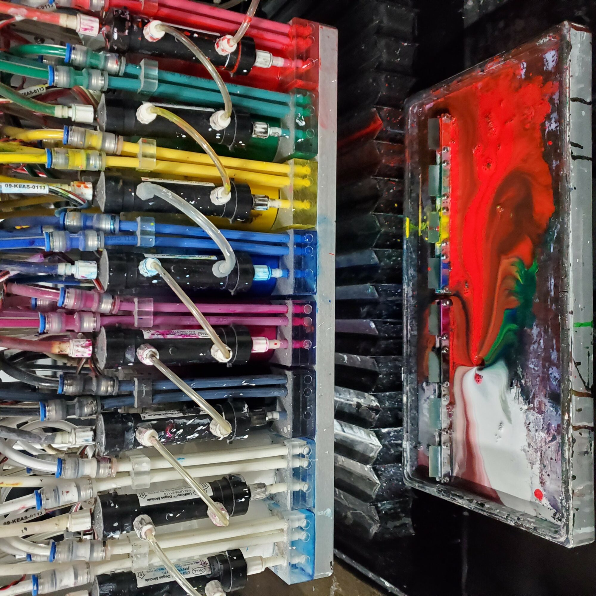 Colorful wires connected to a panel with various colored cables, next to a paint-splattered box with red, green, and white paint.