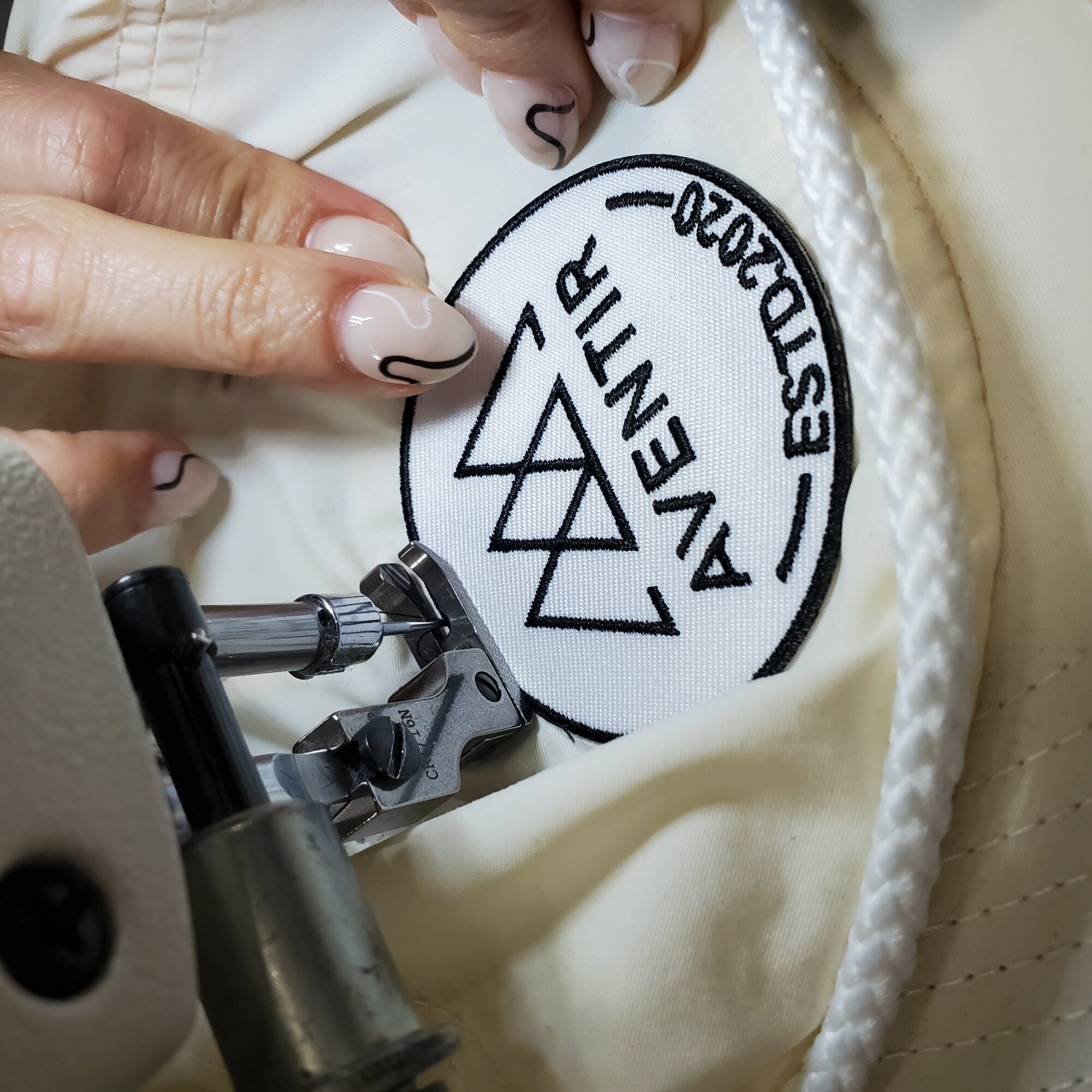 Close-up of a person's hand with painted nails pointing at a fabric label reading 'Avent' and 'BESPOKE'.