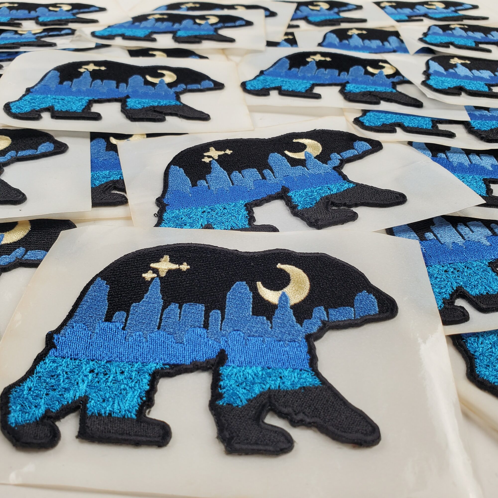 Multiple embroidered patches of a black wolf with a blue cityscape, moon, and stars, on white background.