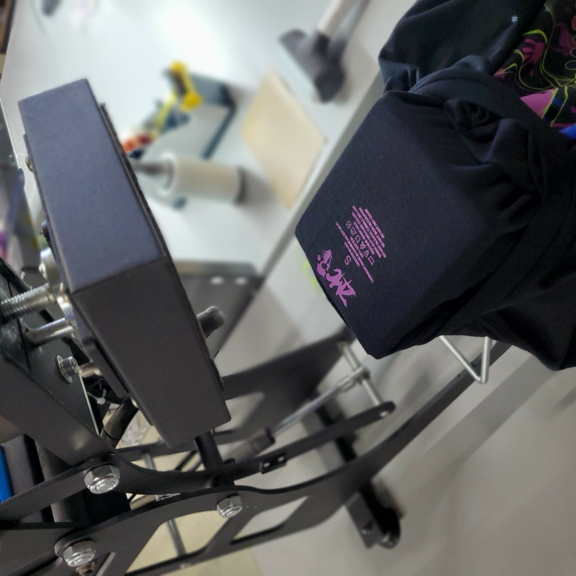 Black bag with purple text on a chair, with a black jacket nearby, in a room with various objects in the background.