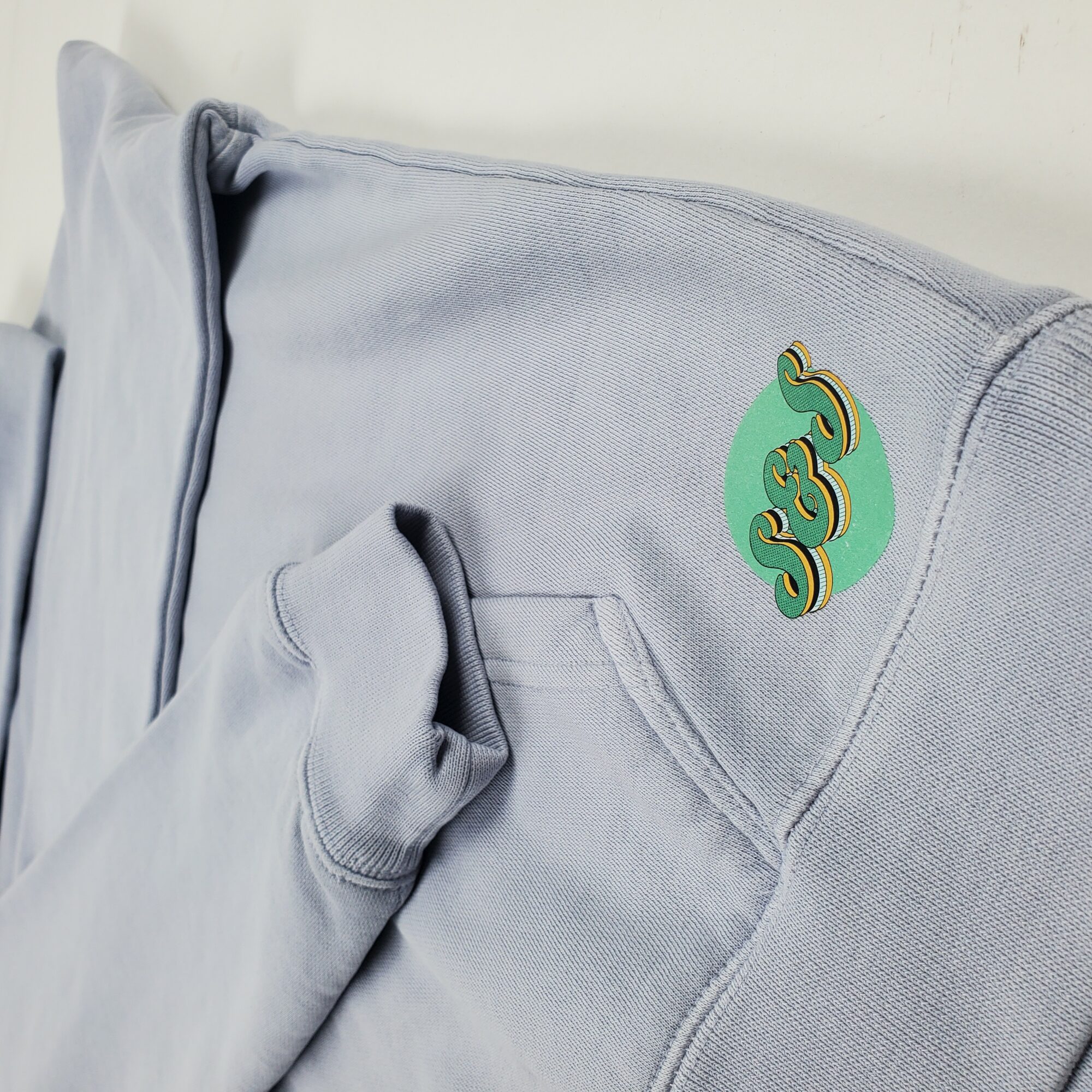 Light gray hoodie with a small, colorful logo on the shoulder, featuring a stylized design in green, yellow, and black.