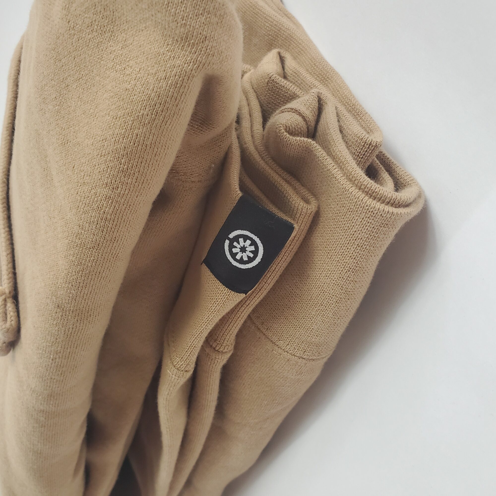 Folded beige clothing with a black circular logo, on a white surface.