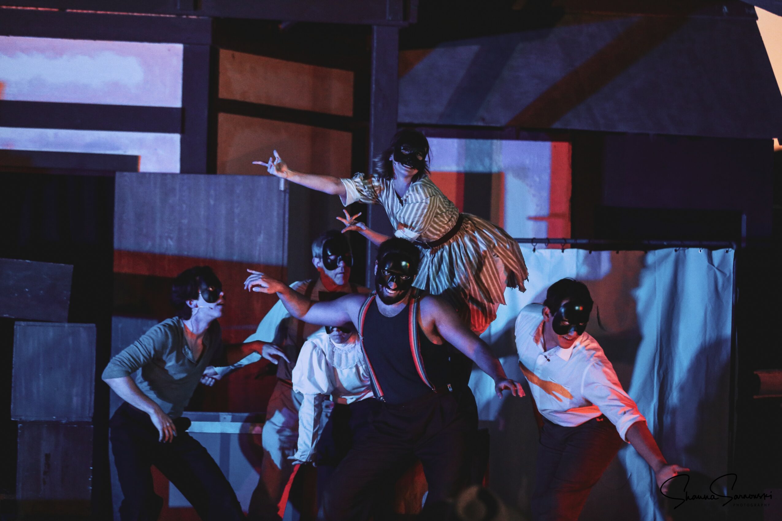 Group of children performing on stage with colorful background, some reaching out and dancing, wearing casual clothes.