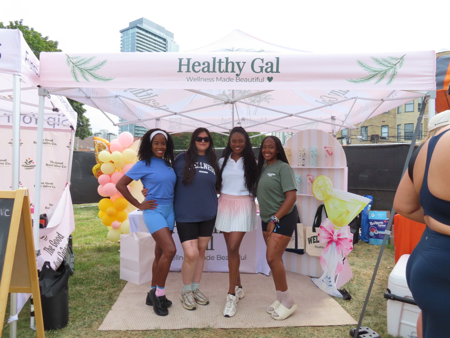 Four women stand together under a tent with balloons and banners at an outdoor event.