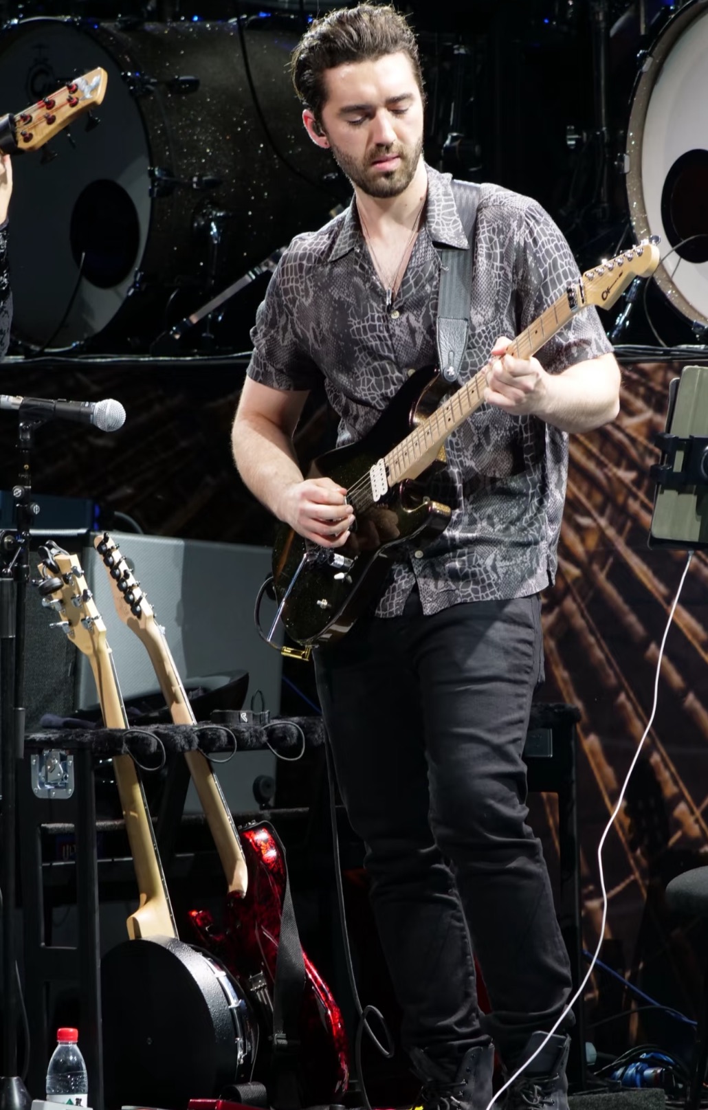 Man playing electric guitar on stage with musical equipment around him.