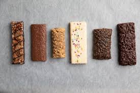 Six rectangular dessert bars with different toppings and textures arranged in a row on a gray surface.