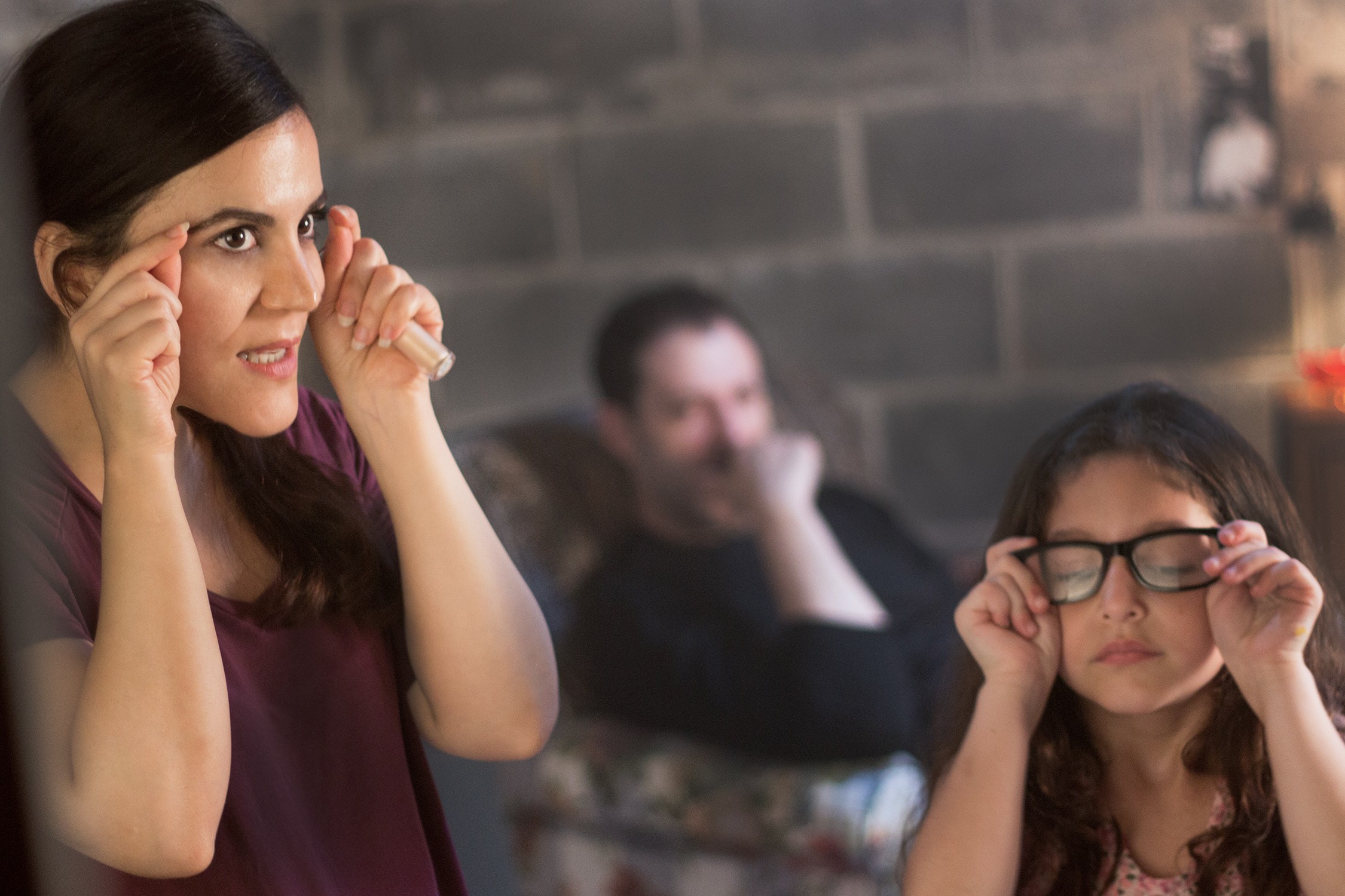 Woman adjusting glasses, girl with glasses, person in background, indoor setting, brick wall, casual atmosphere