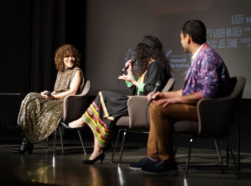 Four people seated on stage, one woman speaking into a microphone, others listening, in a panel discussion setting.