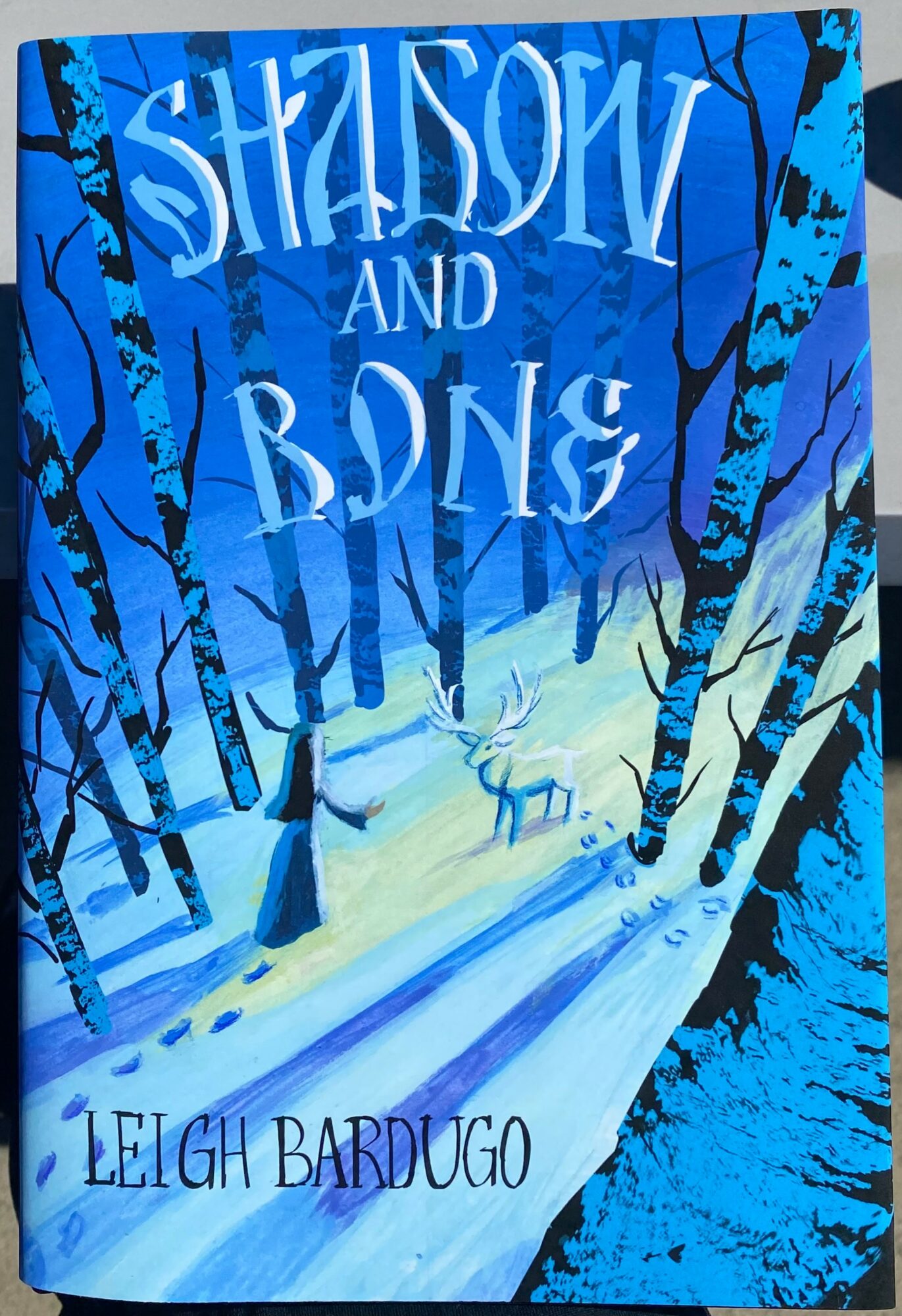 Book cover with a snowy forest scene and a deer, titled 'Shadows and Bones' by Leigh Bardugo.