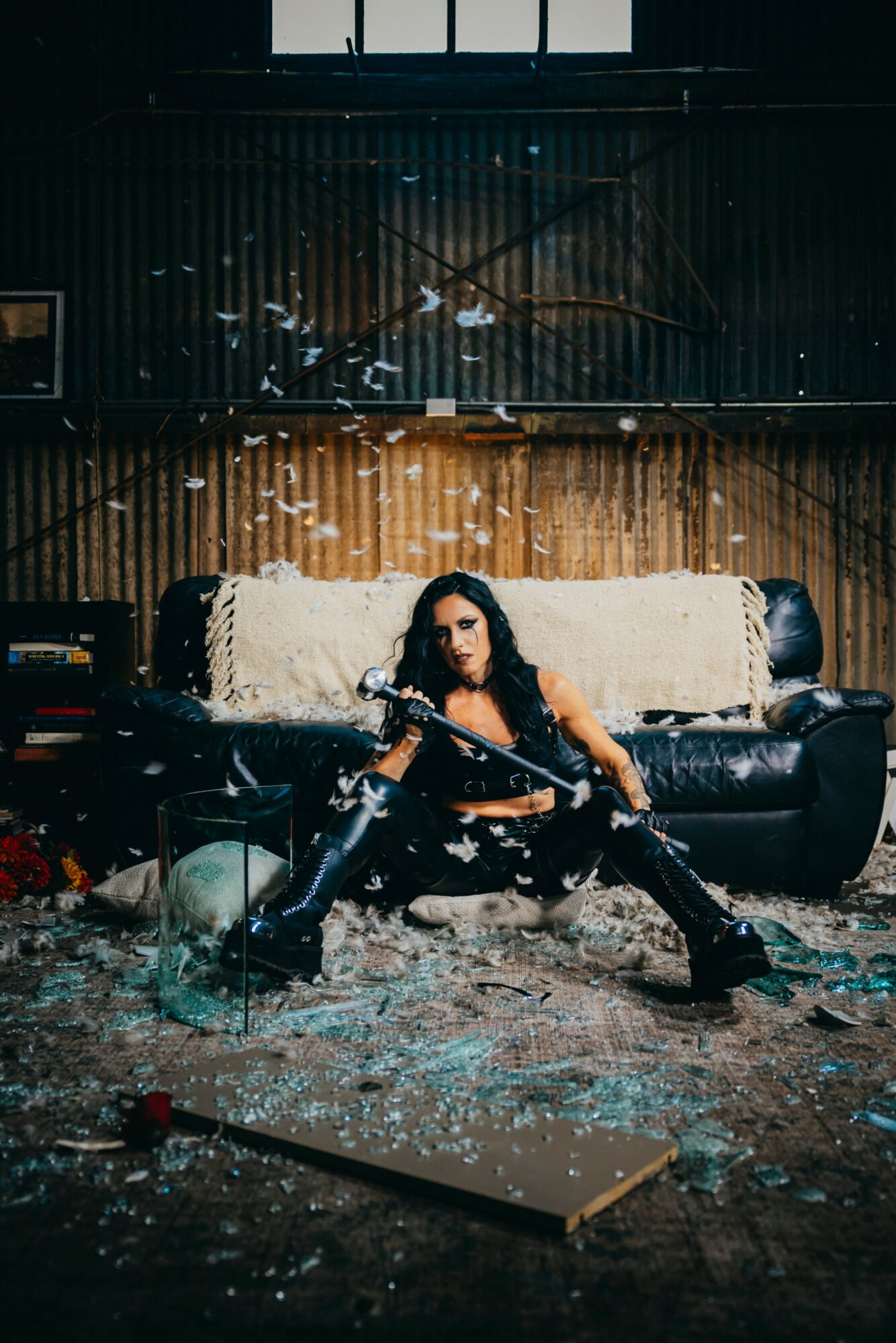 Woman sitting on a damaged sofa holding a gun in an industrial setting with debris and broken glass.