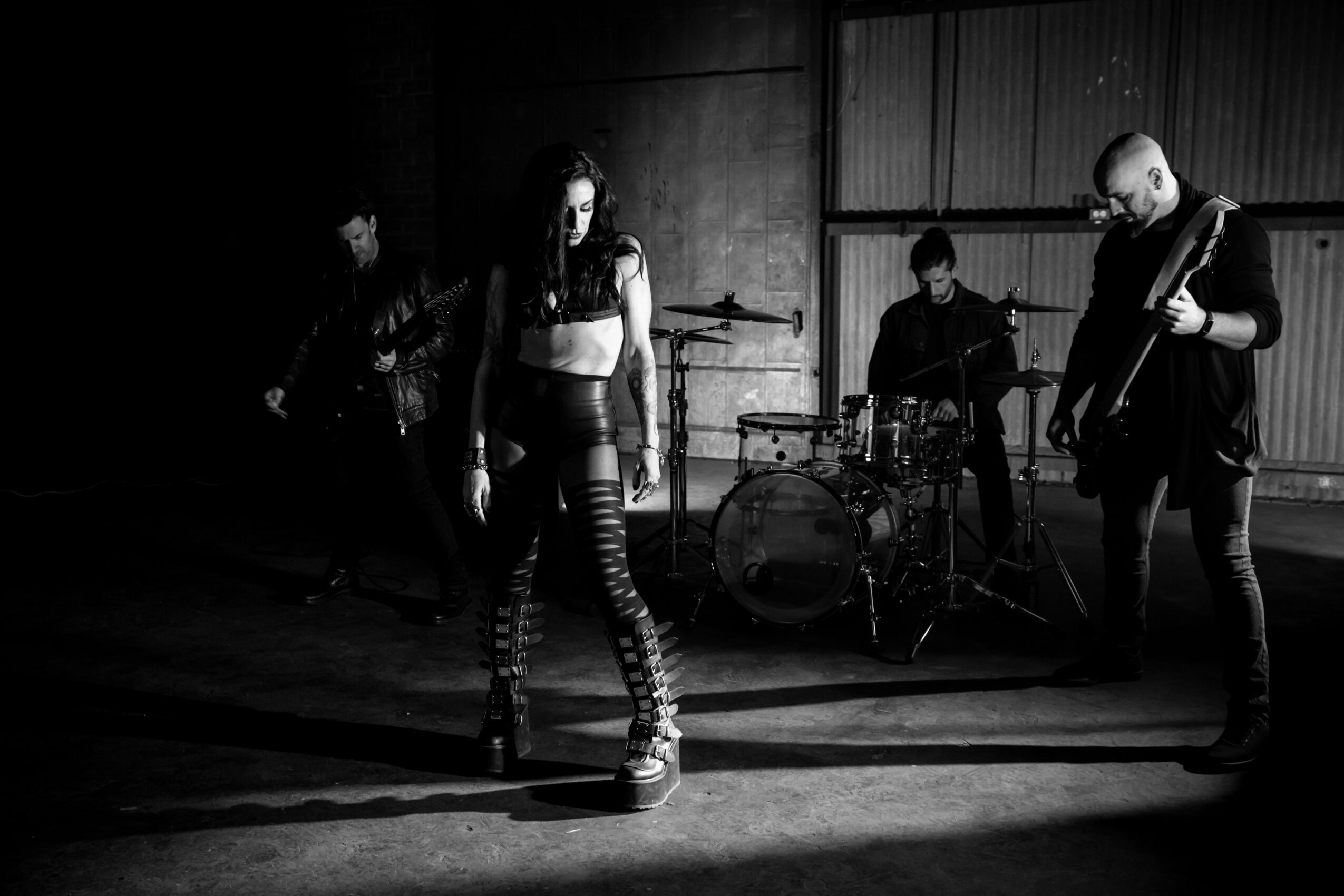 Four musicians perform on stage with a female singer in the center, playing instruments in a dark setting.