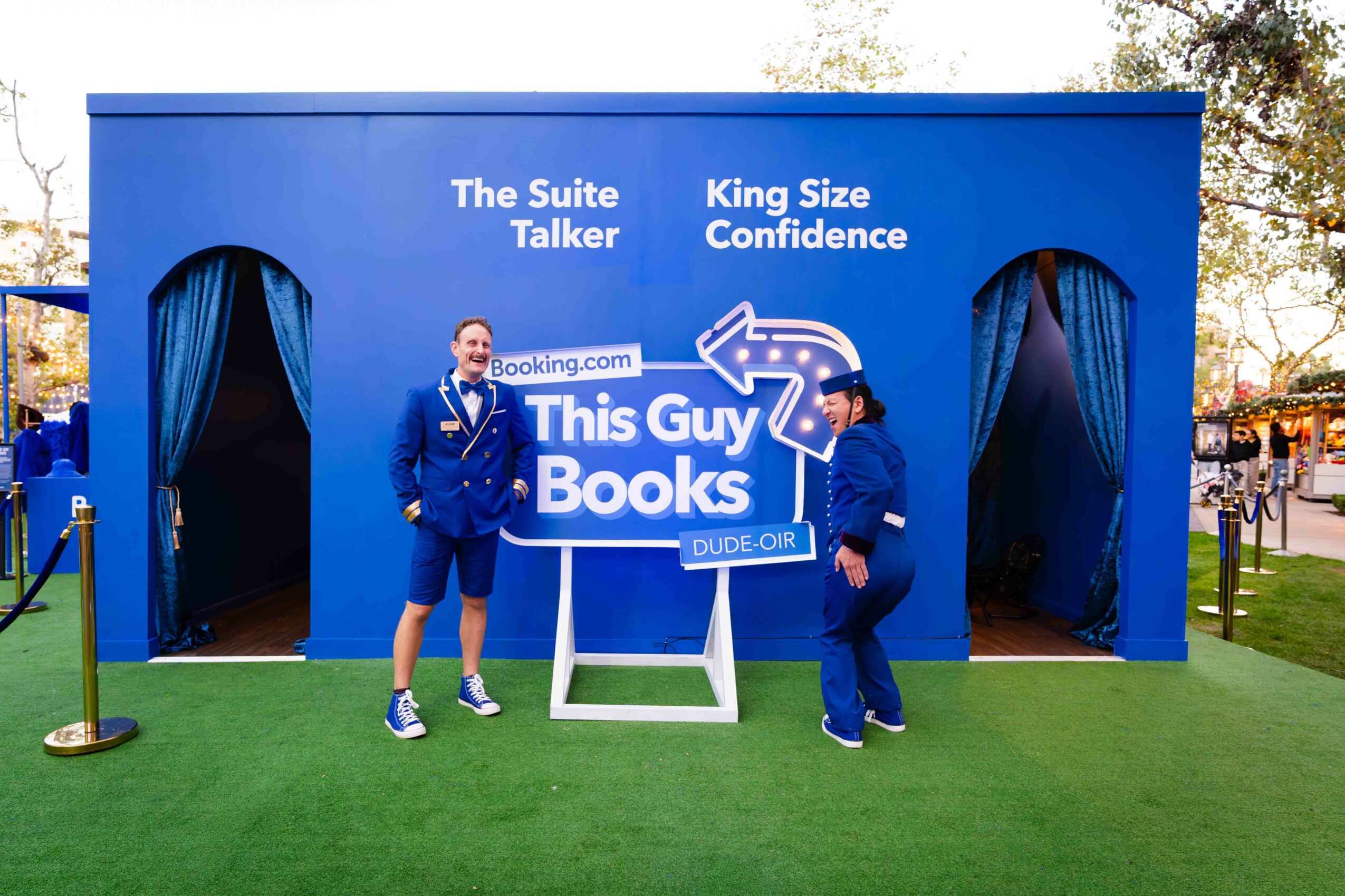 Two men in blue suits stand in front of a book-themed booth with a sign reading
