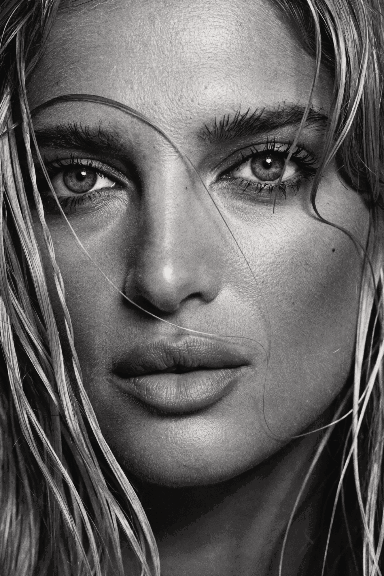 Close-up of a woman's face with wet hair, intense eyes, and full lips, in black and white.