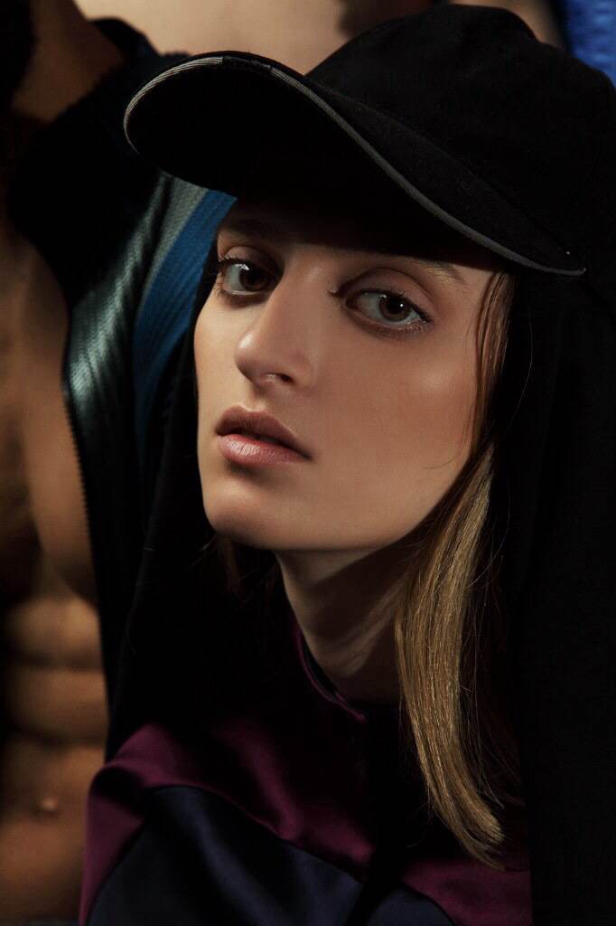 Close-up of a woman wearing a black cap, with a serious expression, dark background, and soft lighting.