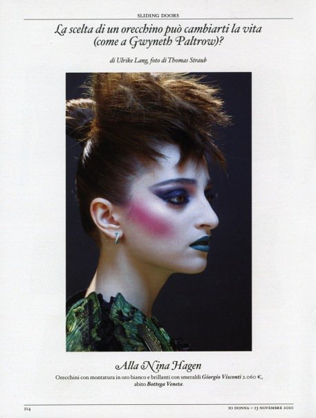 Profile of a woman with dramatic makeup and styled hair, wearing a green lace garment, against a dark background.