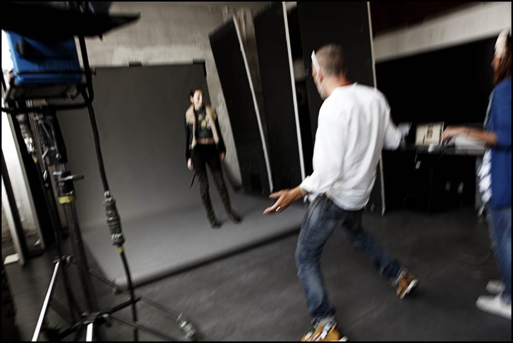 Person in white shirt and jeans dancing in a studio with a woman in black and another person in blue nearby.
