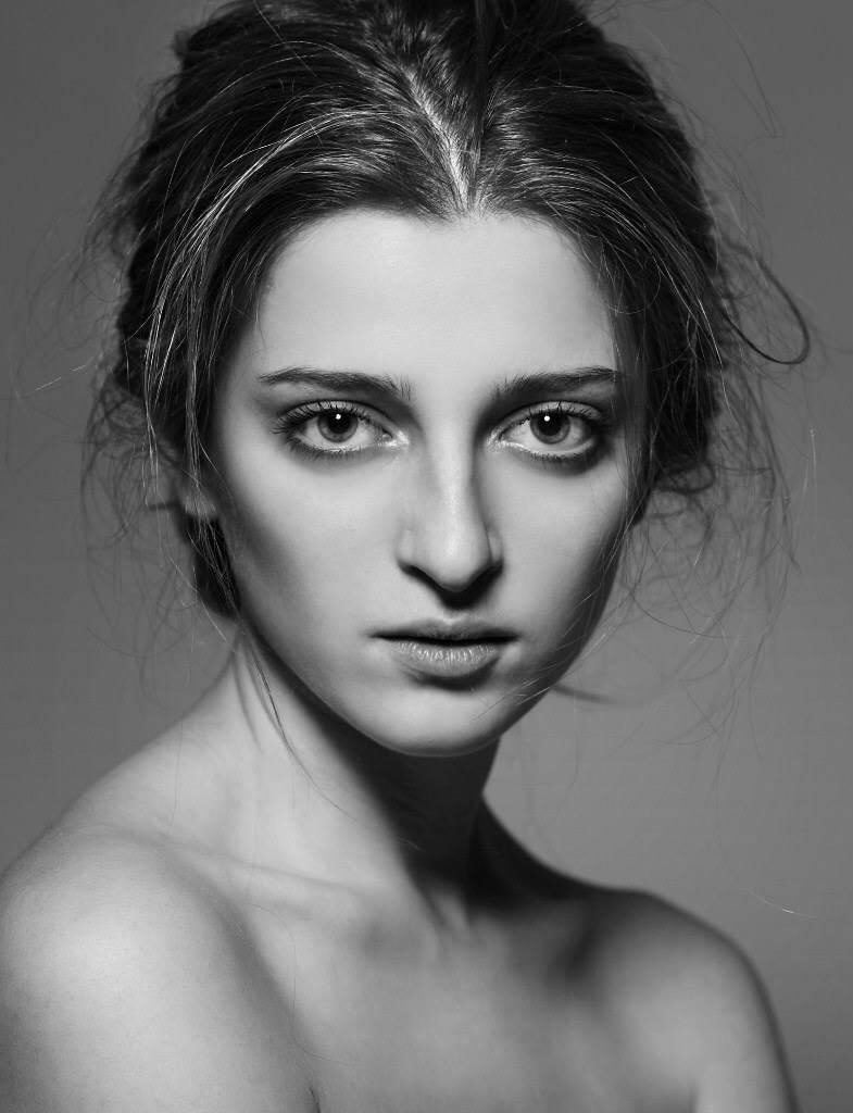 Black and white portrait of a woman with tousled hair, intense gaze, and bare shoulders.