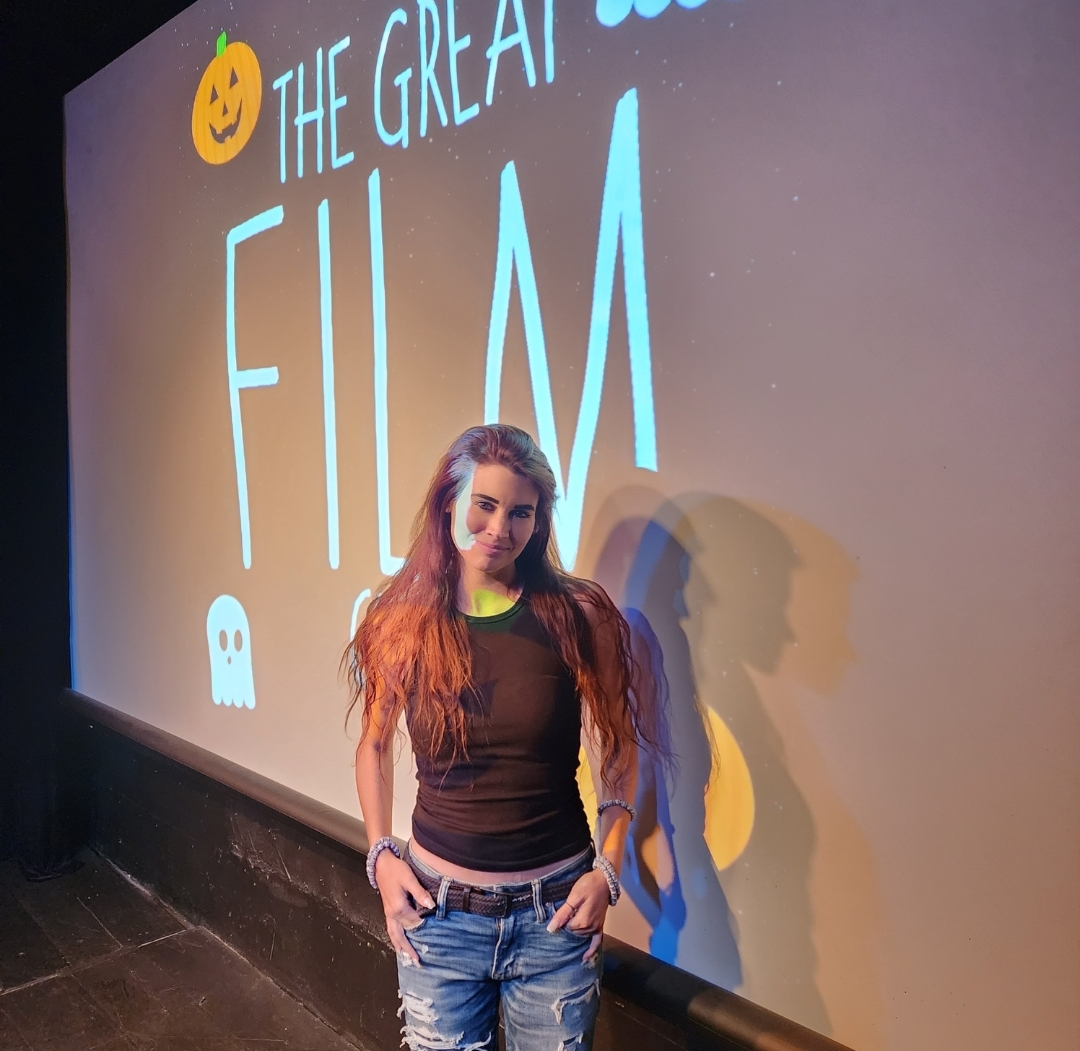 Young woman with long hair standing in front of a screen displaying text and graphics, including a pumpkin and ghost icon.
