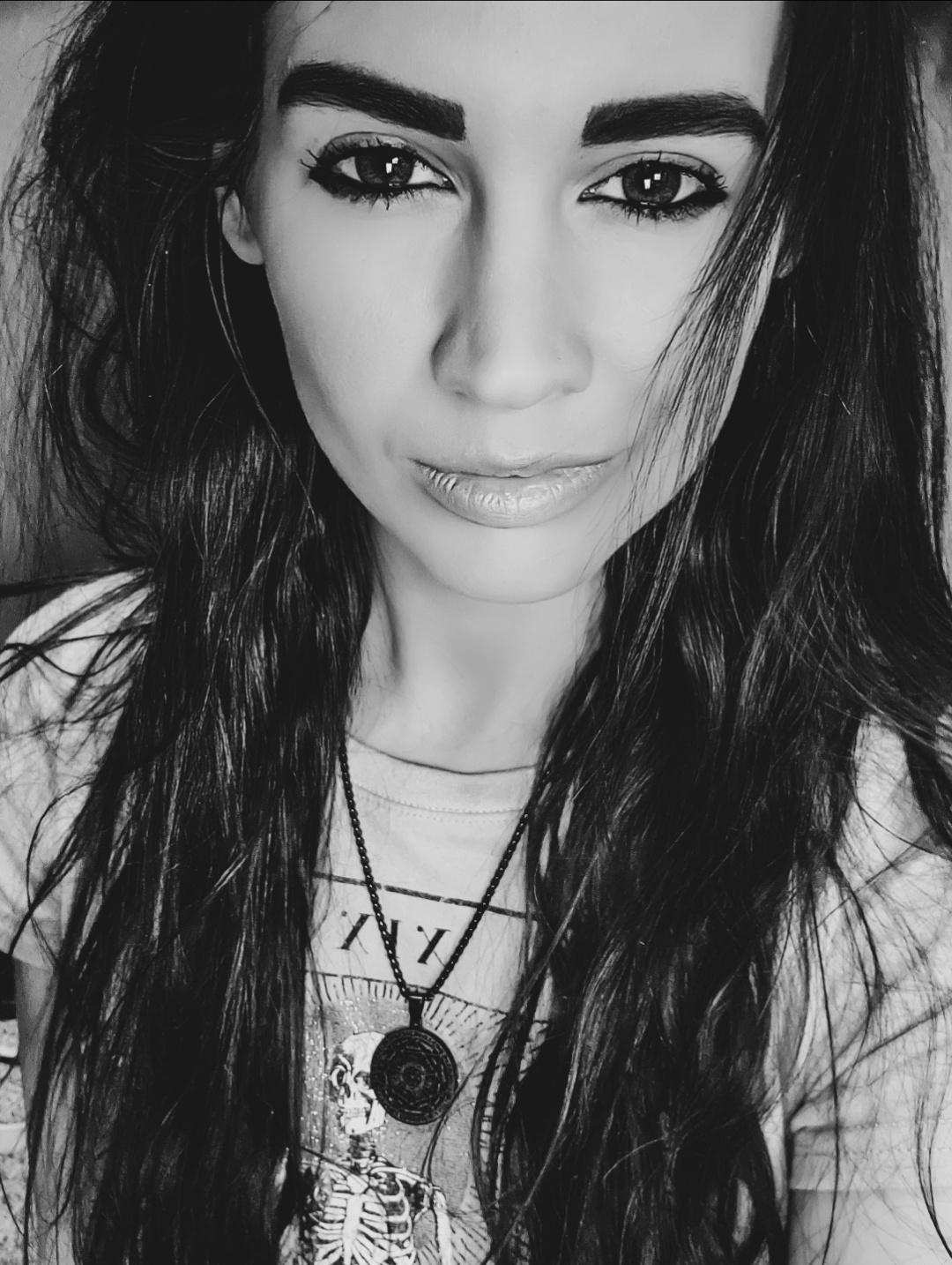 Black and white portrait of a woman with long wavy hair, dark eyebrows, and a subtle smile, looking directly at the camera.