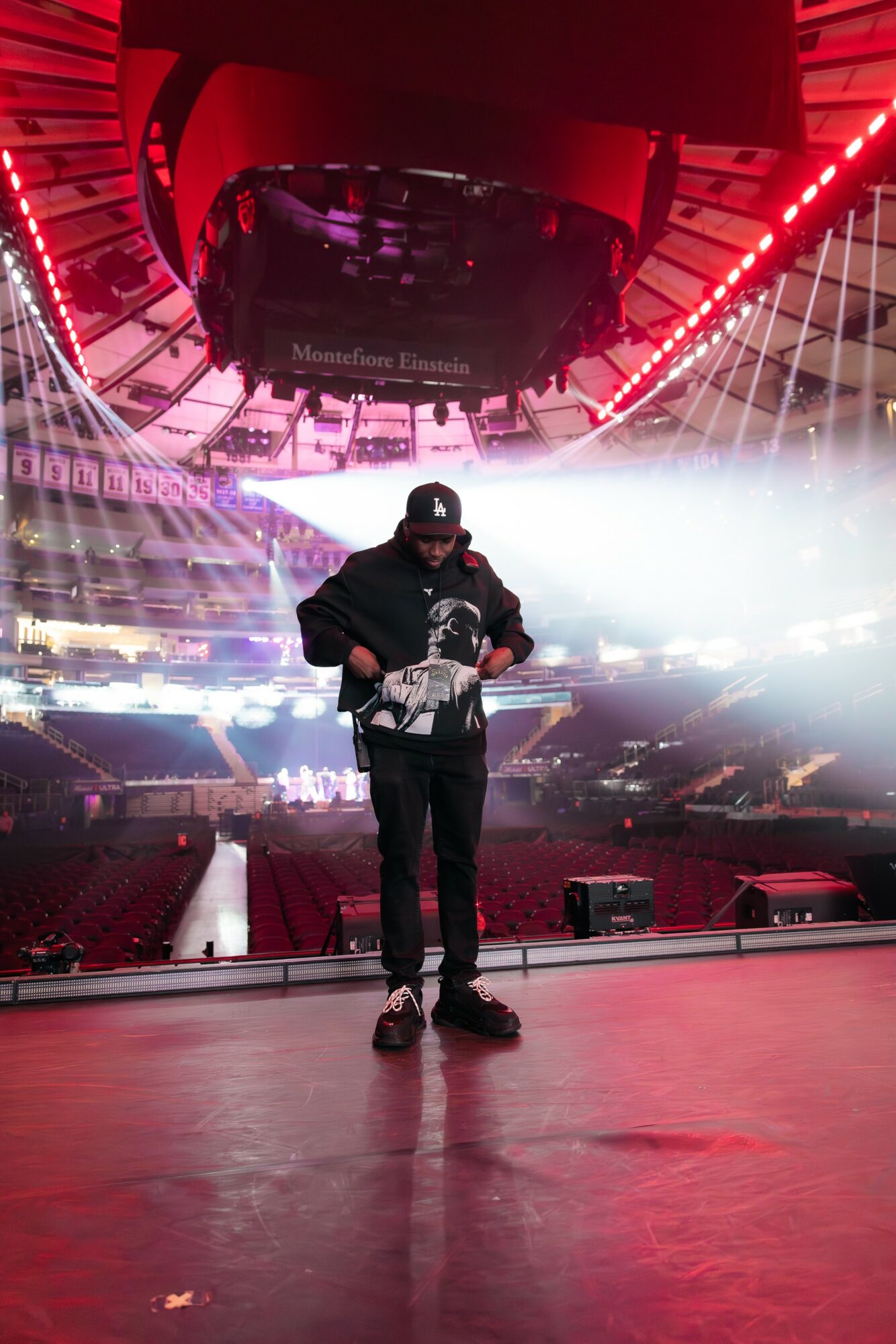 Person standing on stage in an arena with bright lights and a large circular screen overhead.