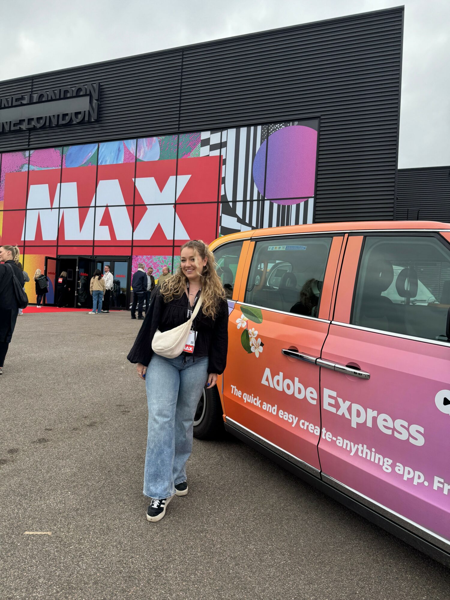 Person standing next to a pink and orange vehicle with a large Adobe Express logo on a building in the background.