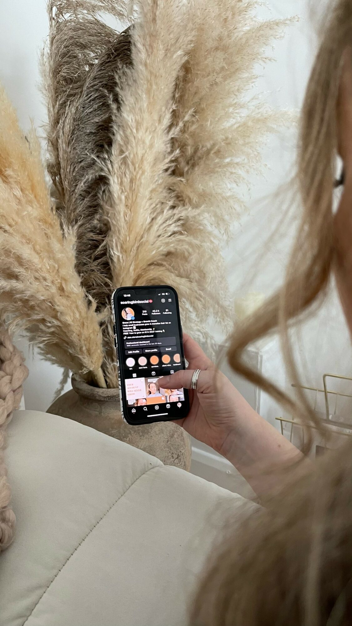 Person holding a smartphone with a social media app, standing next to a large, fluffy, beige-colored animal with long fur.