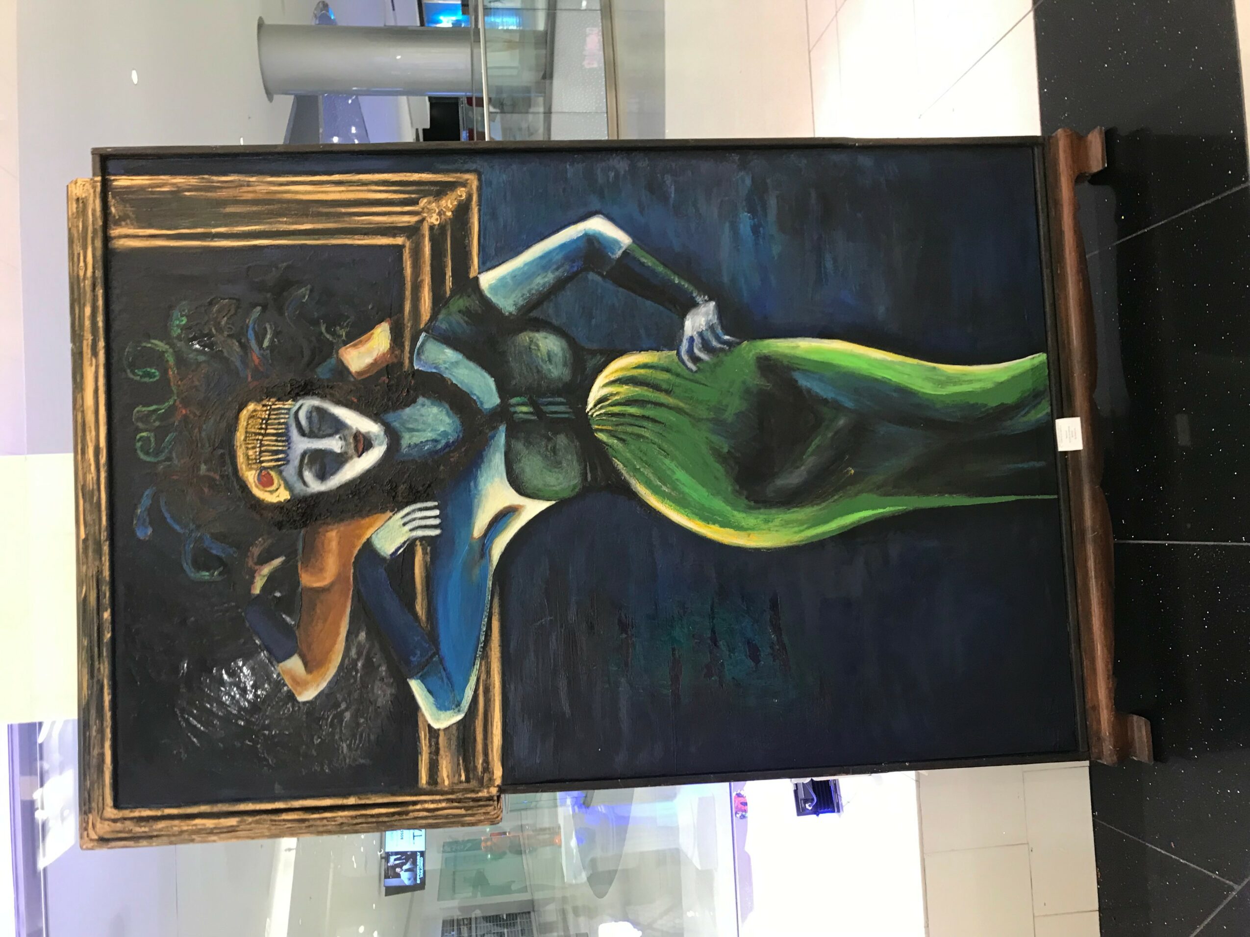 Painting of a woman with a green dress, standing in front of a mirror, with a dark background and gold frame.