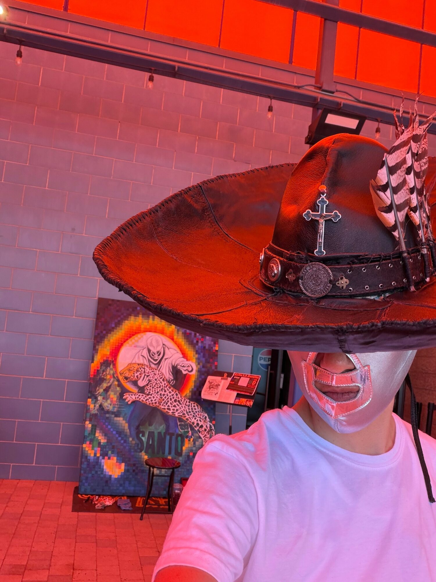 Person wearing a white shirt and face mask, with a pirate hat and sword, in front of a colorful painting of a creature.