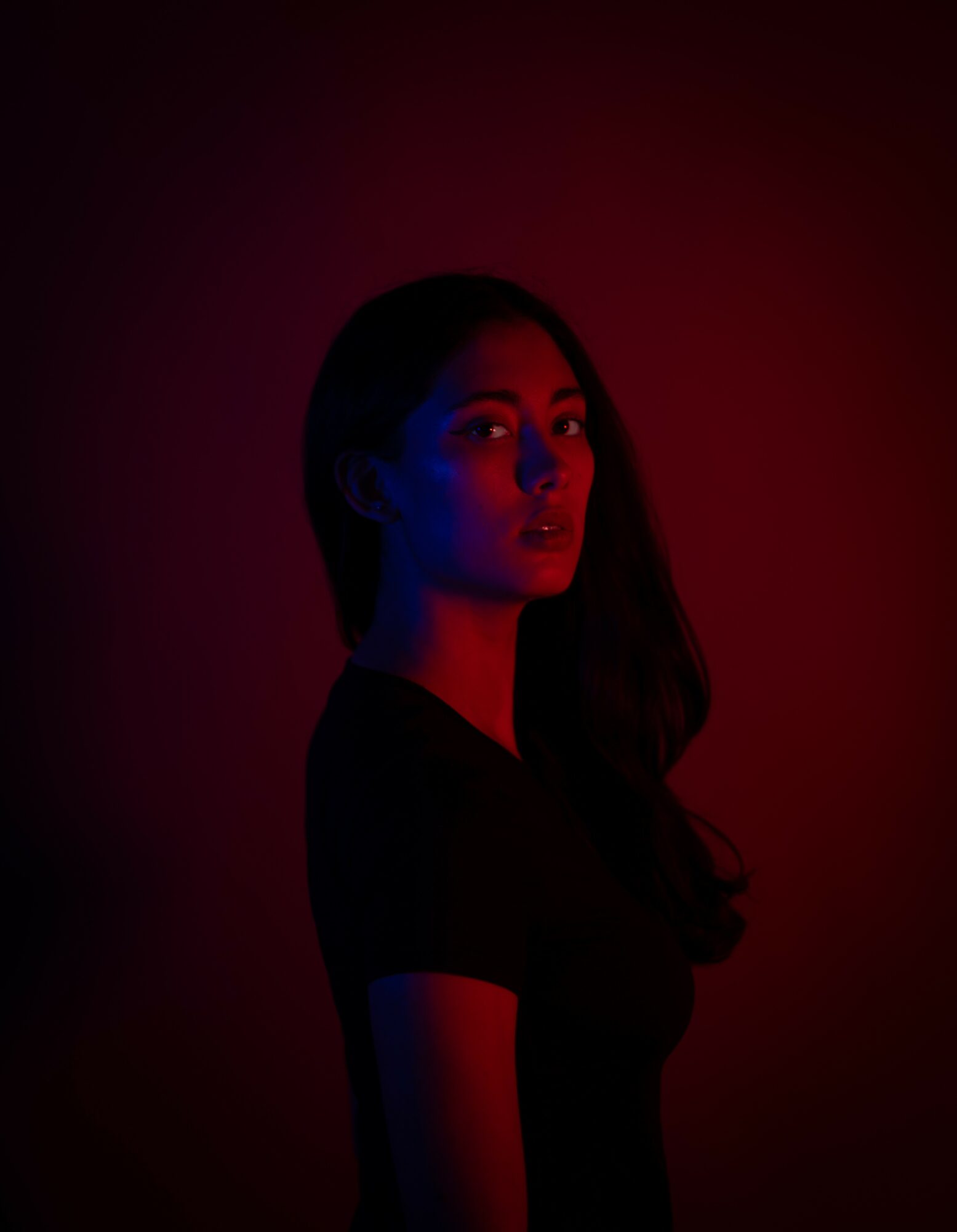 Woman with long hair in dark lighting, illuminated by red and blue lights, facing slightly to the right.
