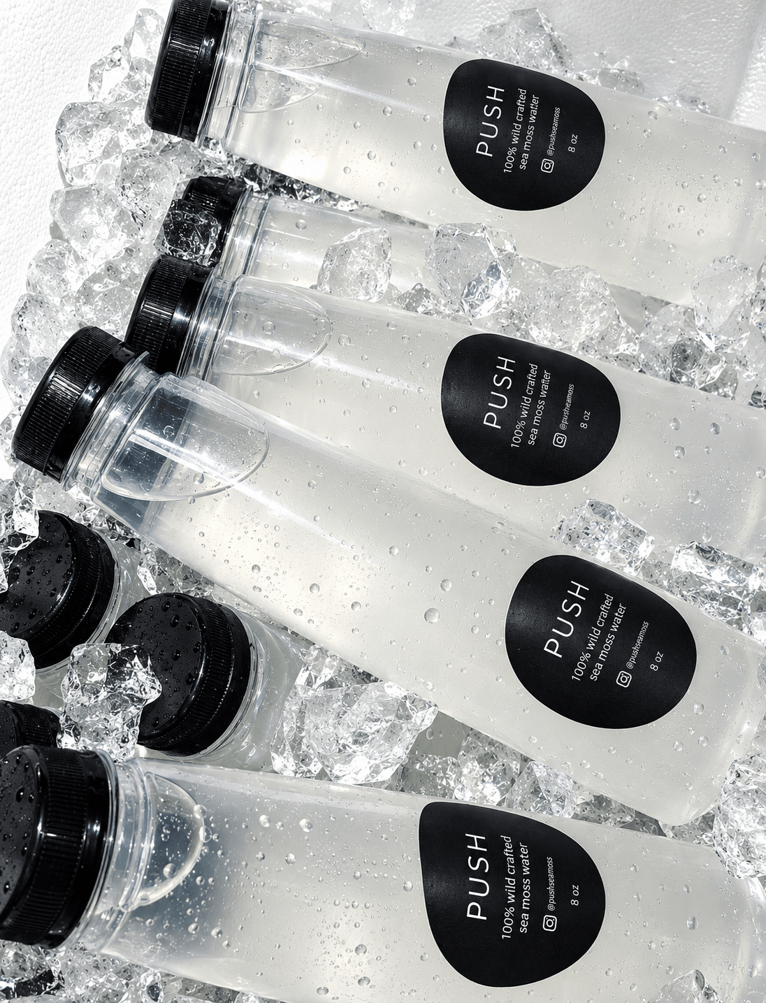 Three clear bottles with black caps and black labels reading 'PUSH' are on ice, with water droplets visible.