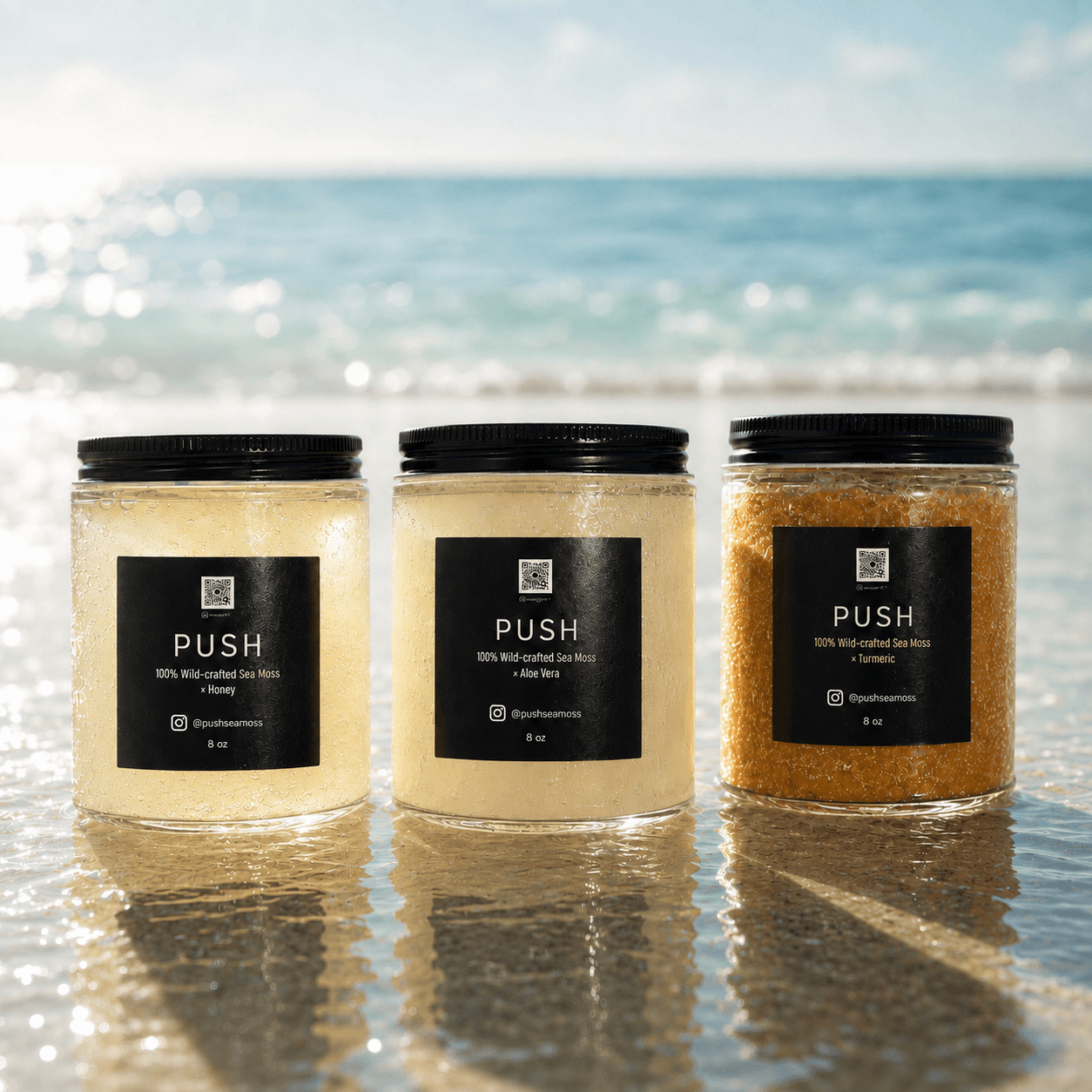 Three jars with black labels are placed on wet sand at the beach, with the ocean and sky in the background.