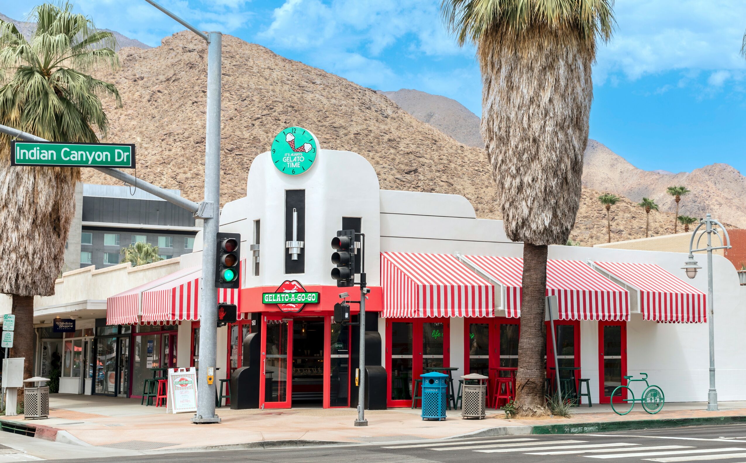 Building with red and white striped awnings, palm trees, mountain background, street sign, and traffic lights.