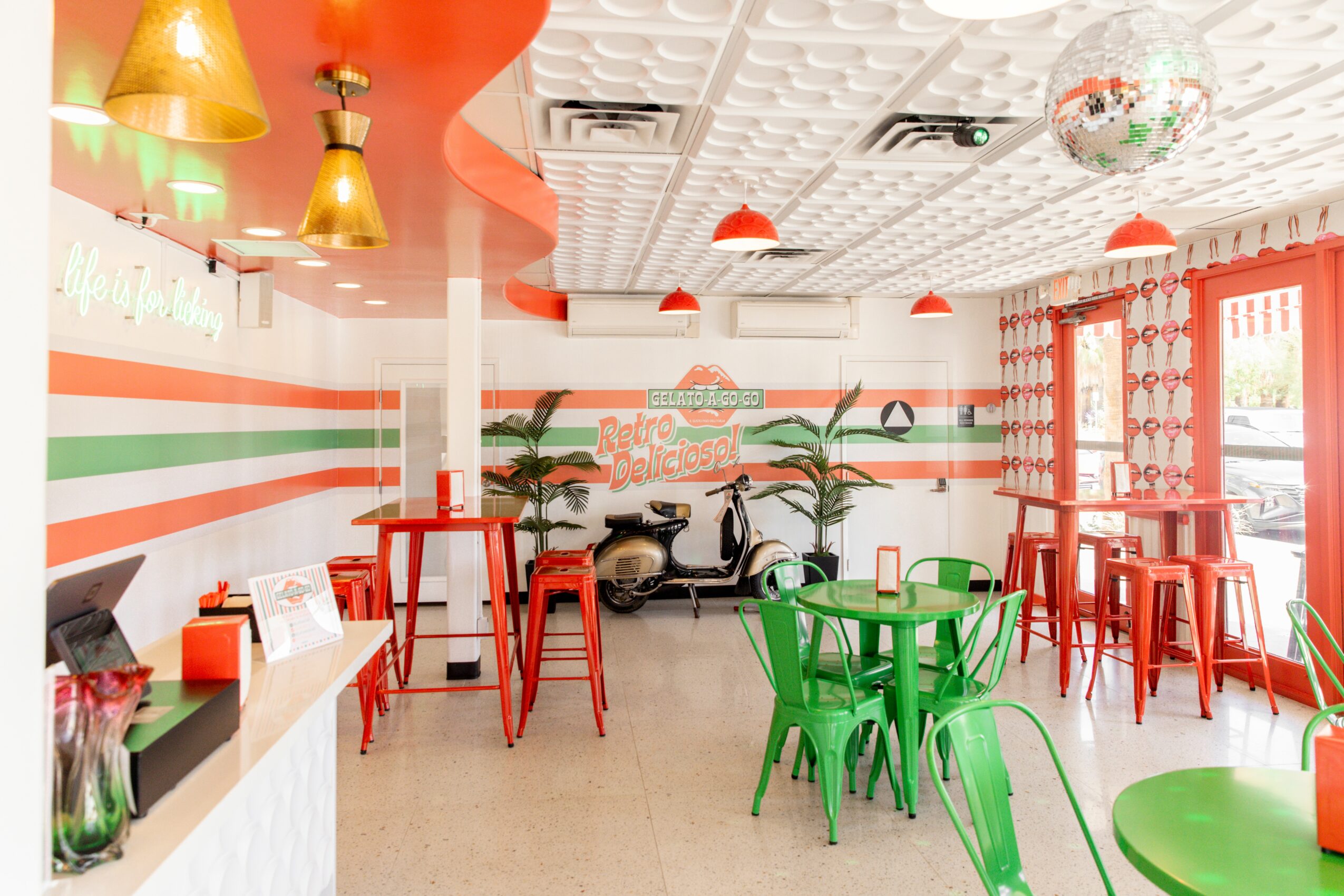 Colorful cafe interior with green and red chairs, striped wall, and decorative ceiling, bright and inviting atmosphere.