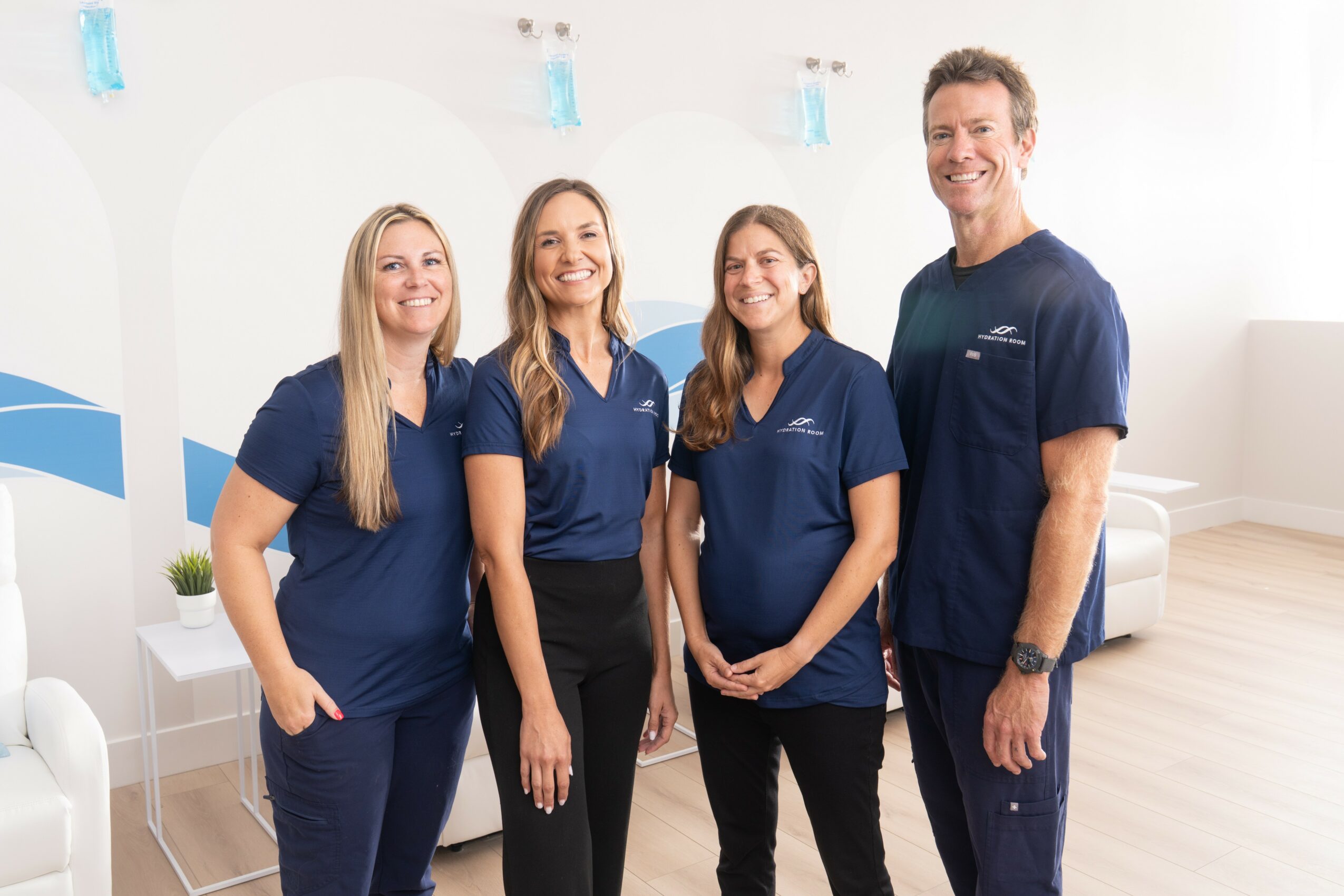 Four healthcare professionals in blue uniforms standing in a bright, modern clinic with white walls and furniture.