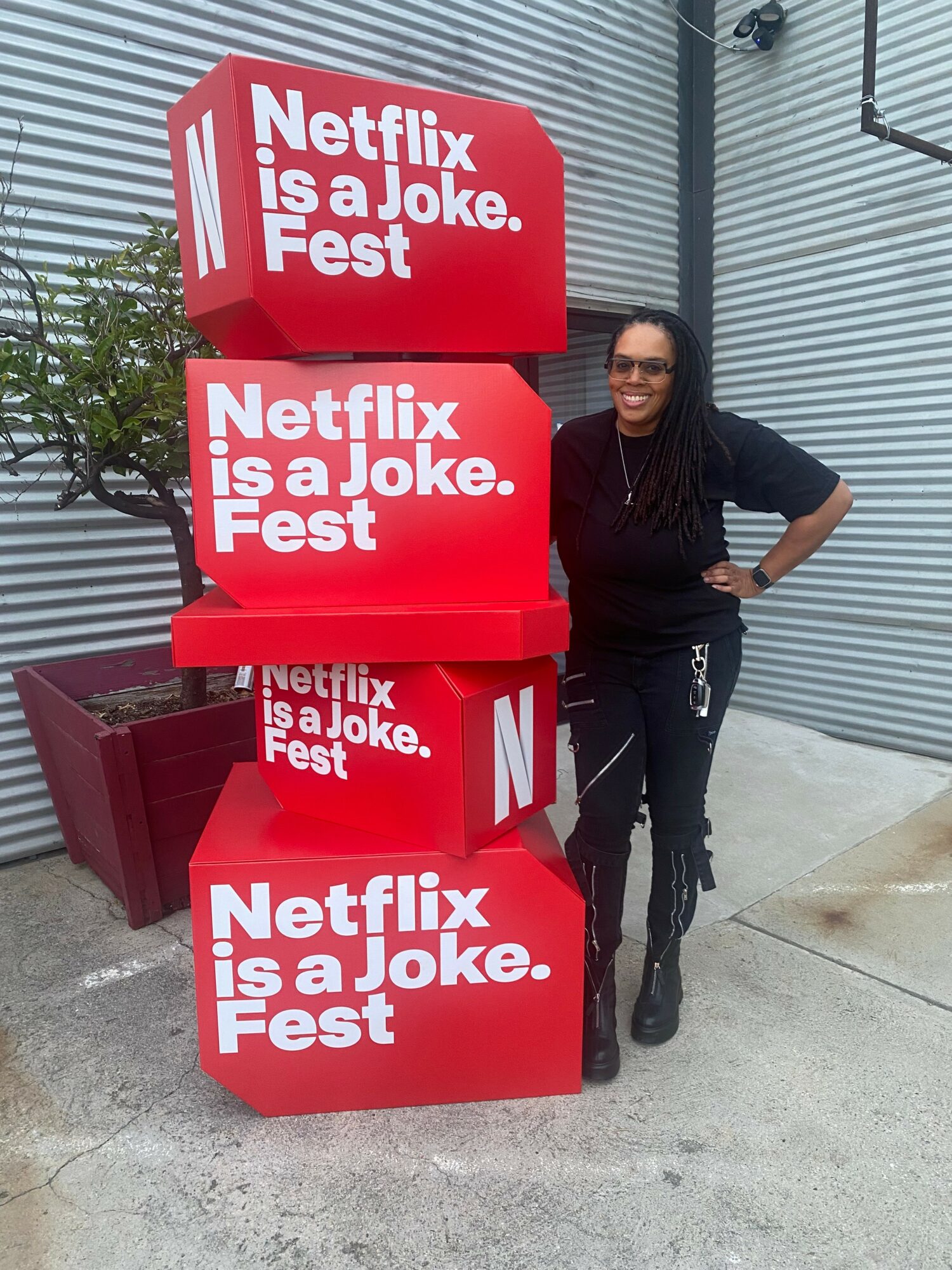 Woman standing next to stacked red signs with white text, outside building with metal siding.