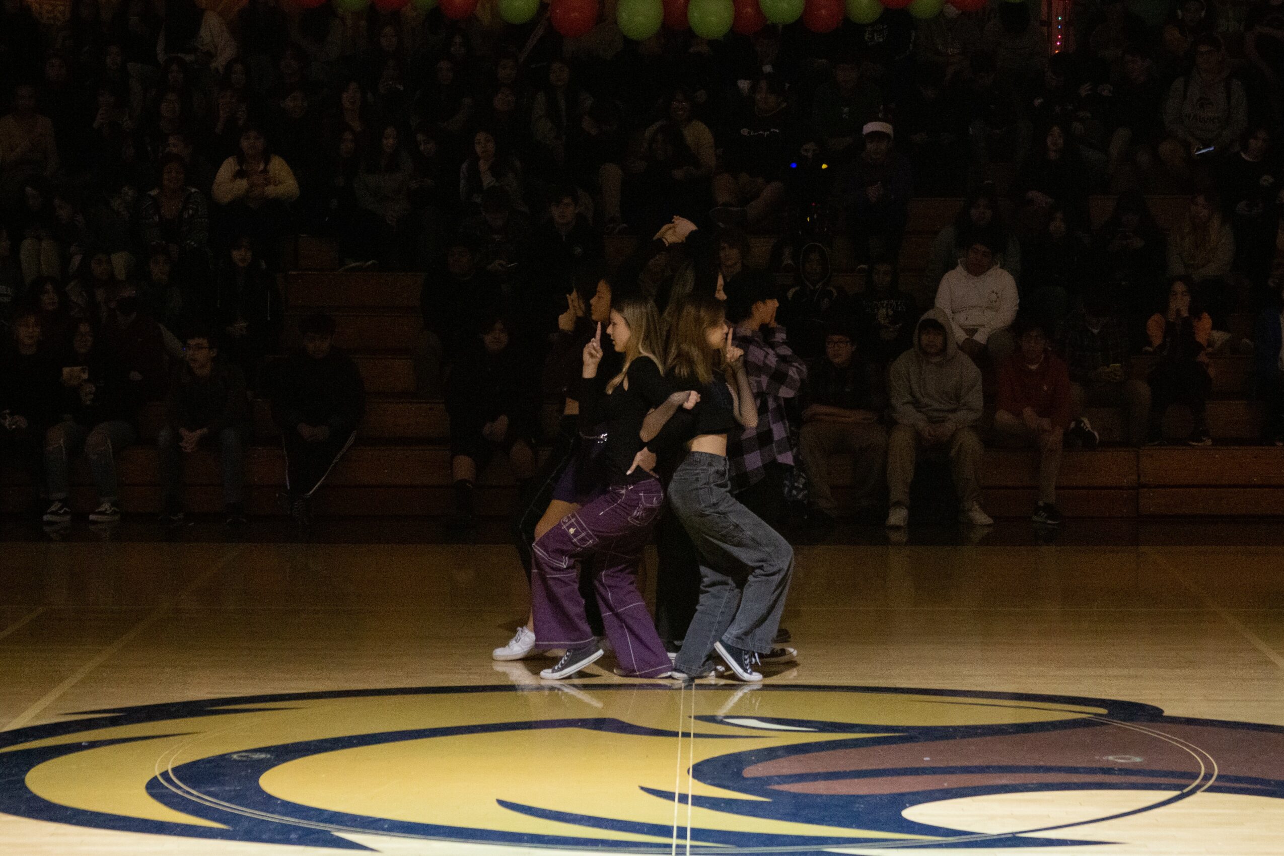 Two people dancing on a basketball court with an audience in the background, with some audience members seated and others standing.