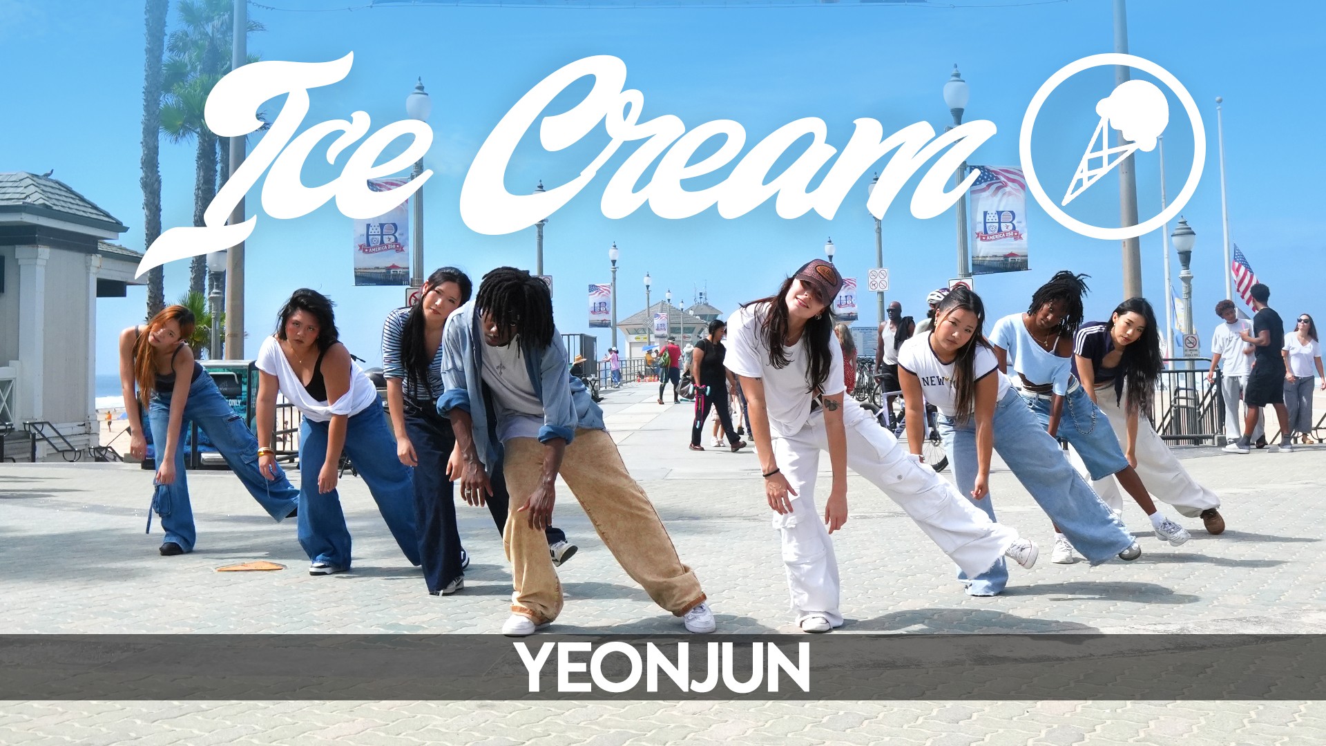 Group of people performing a dance outdoors with a large ice cream sign in the background.