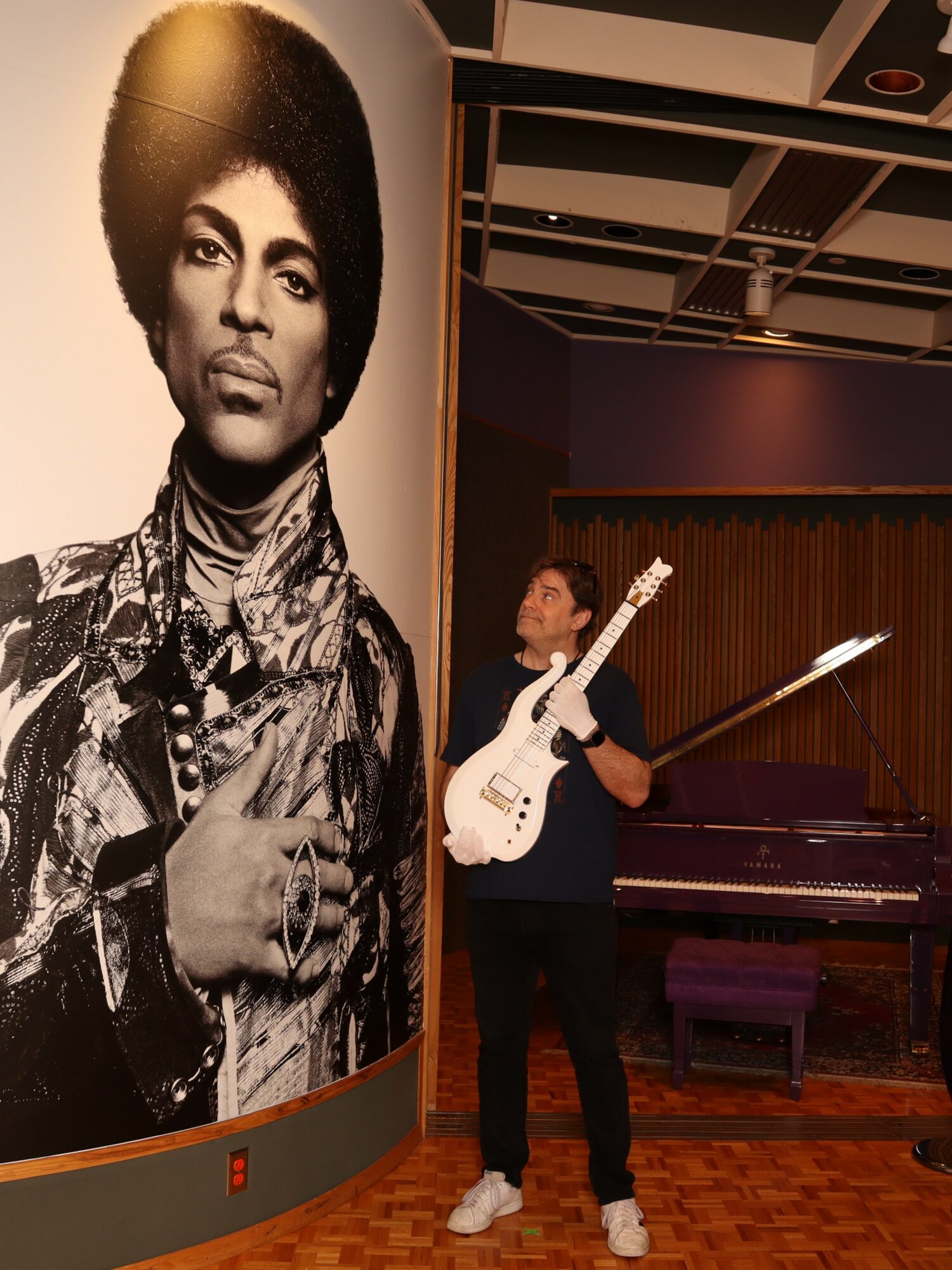 Person holding a guitar in a room with a large black-and-white portrait of a woman with an afro hairstyle.