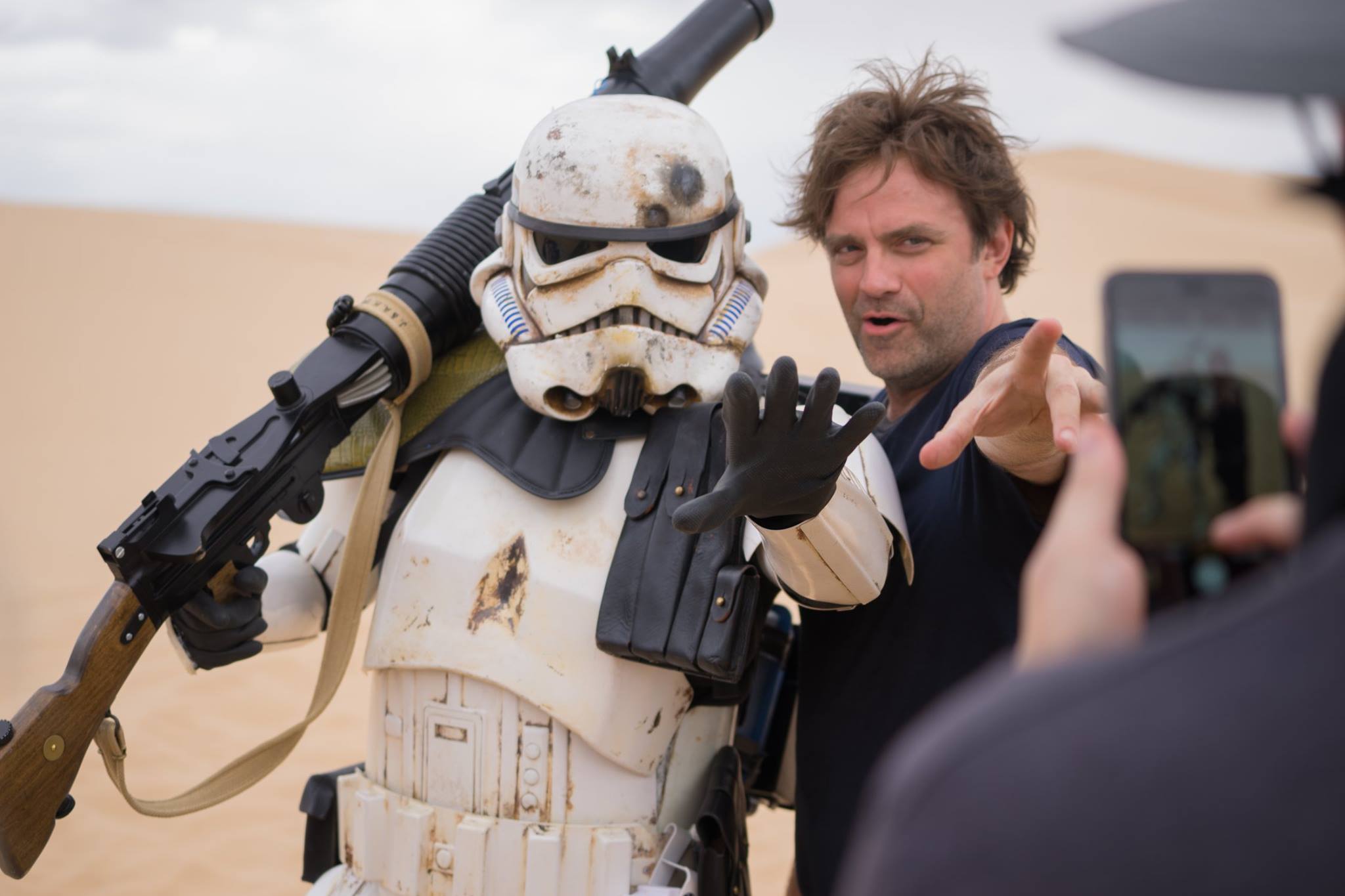 Person in costume as a stormtrooper from Star Wars standing next to a man, with a person taking a photo in the foreground.
