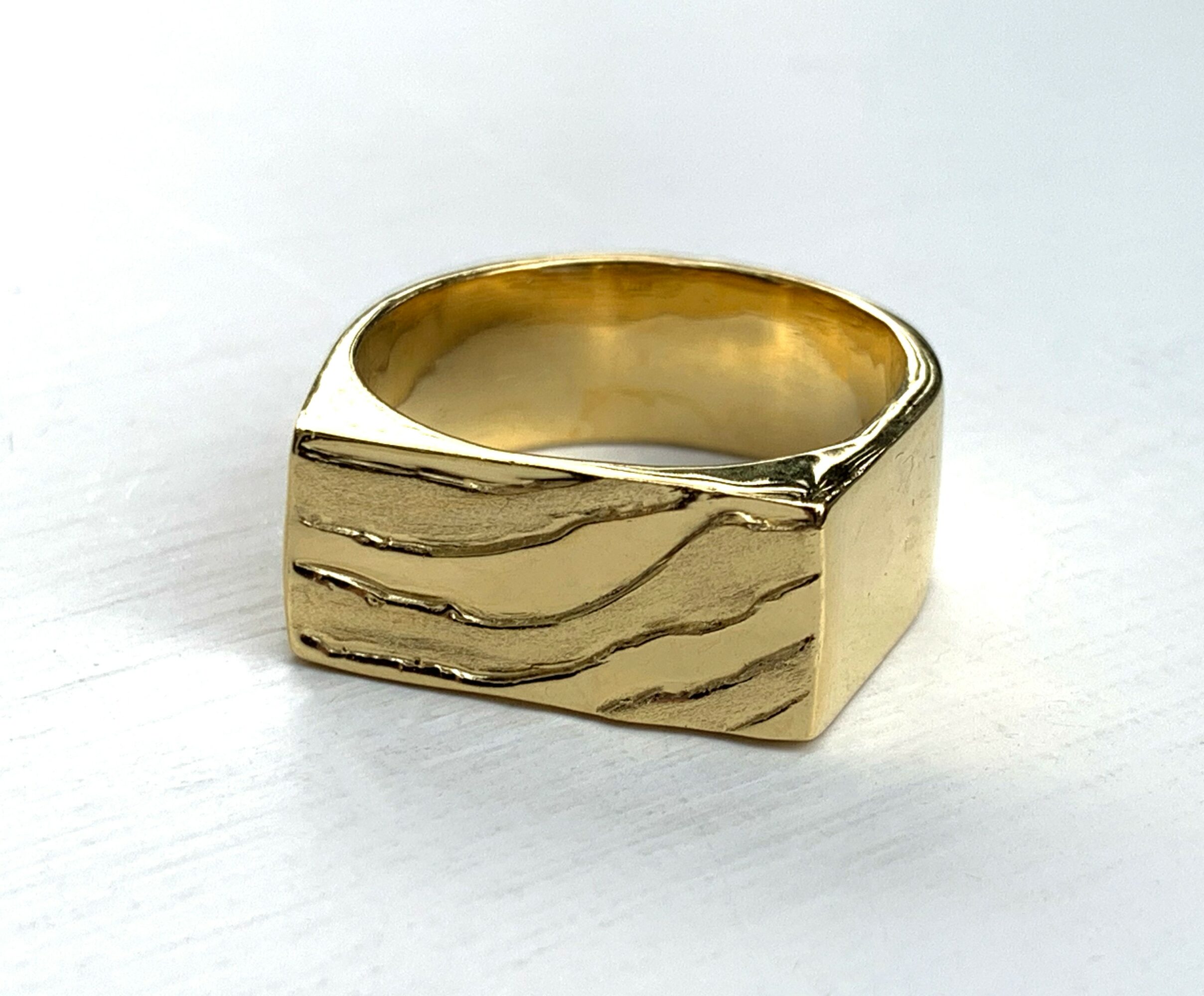 Gold ring with textured surface and irregular shape on a white background.