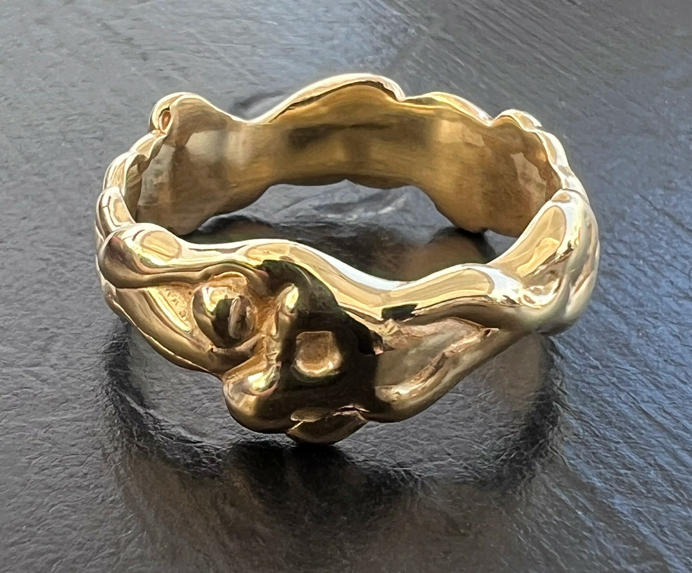 Gold ring with an irregular, organic shape on a dark surface.