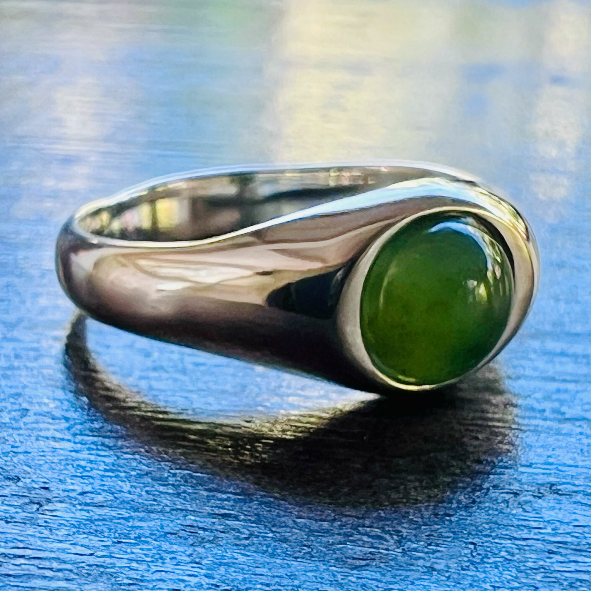 Silver ring with a large green oval stone on a dark wooden surface.