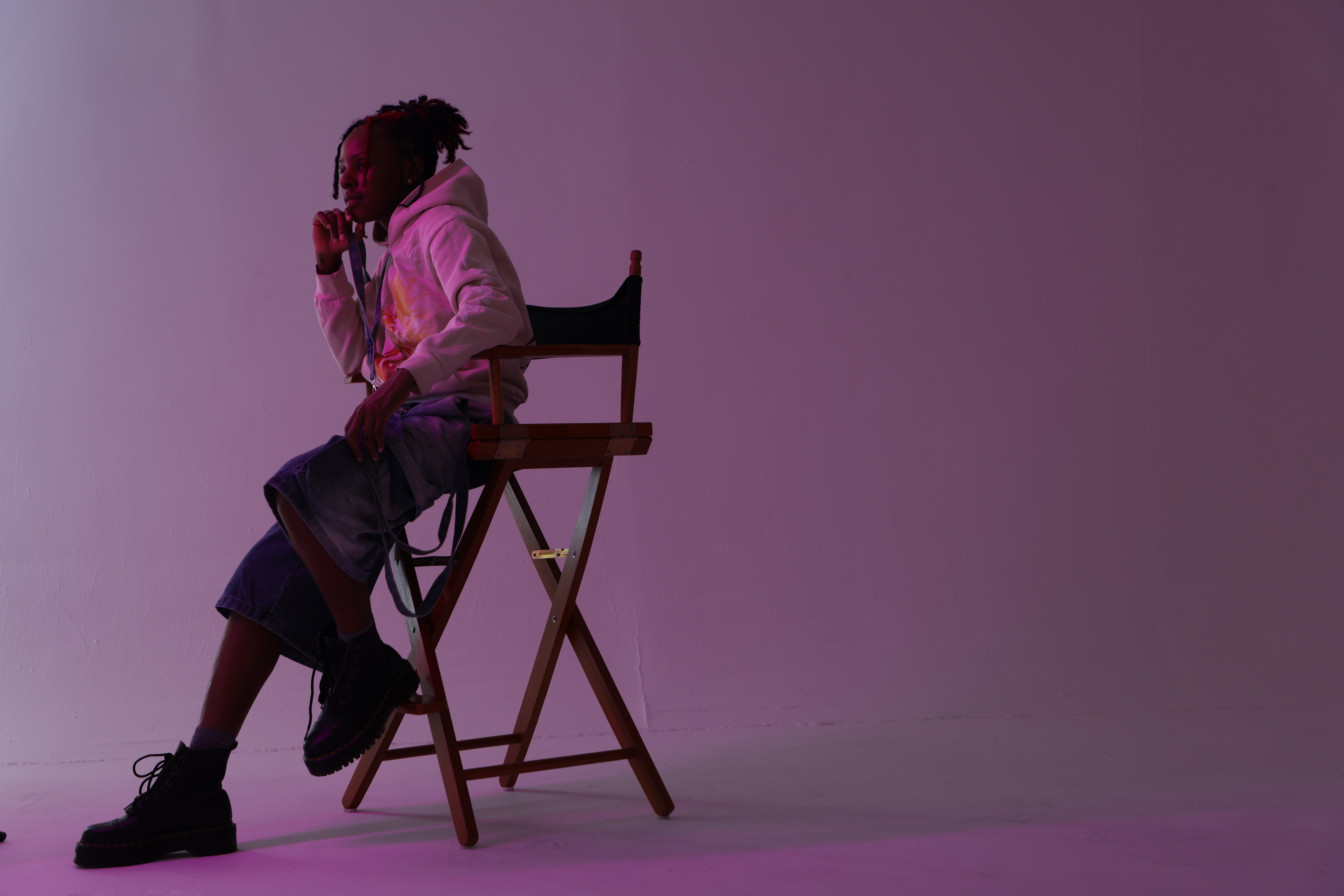 Person sitting on a chair with a small table, against a plain purple background.