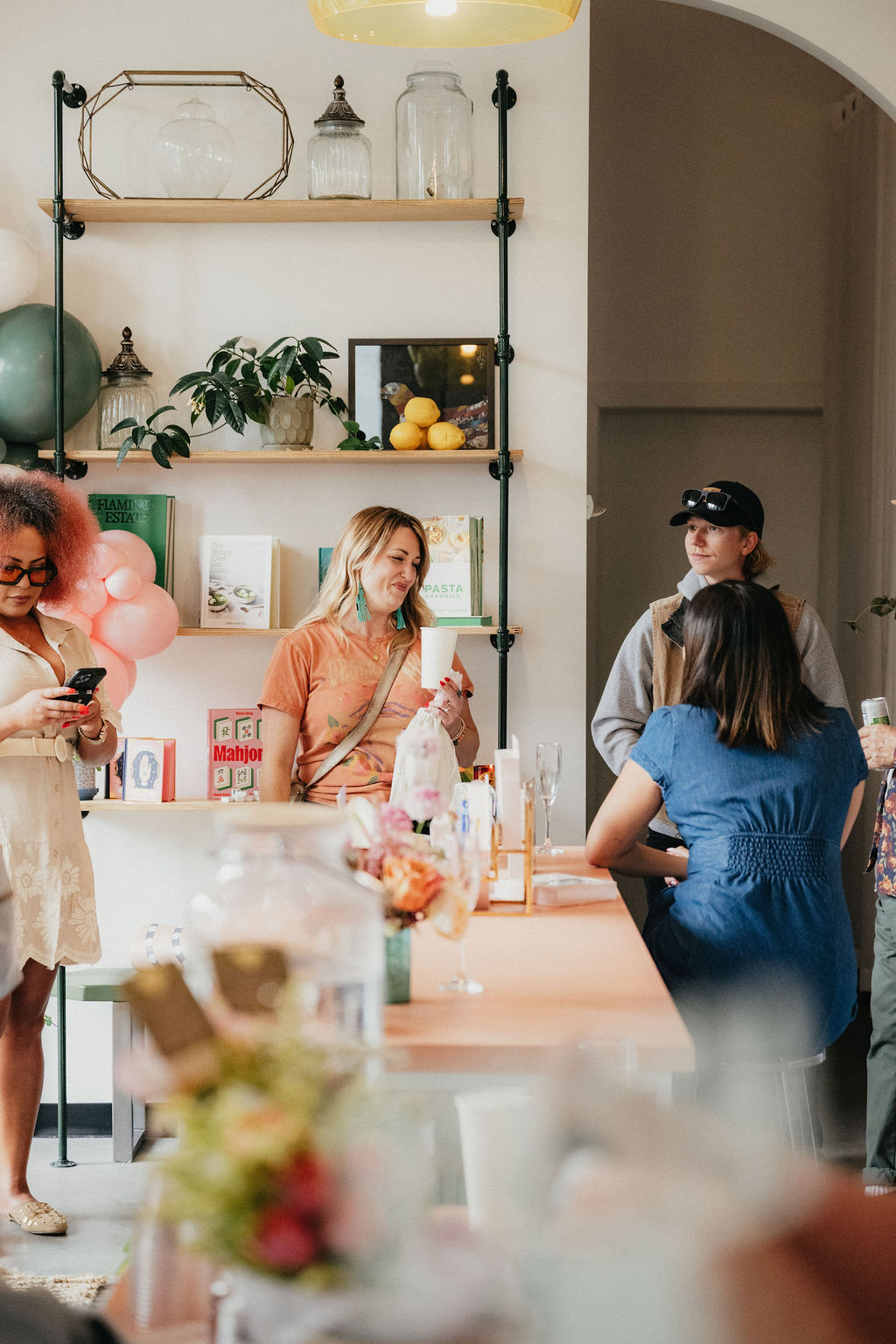 Group of women gathered around a table with decorations and food, engaging in conversation indoors.