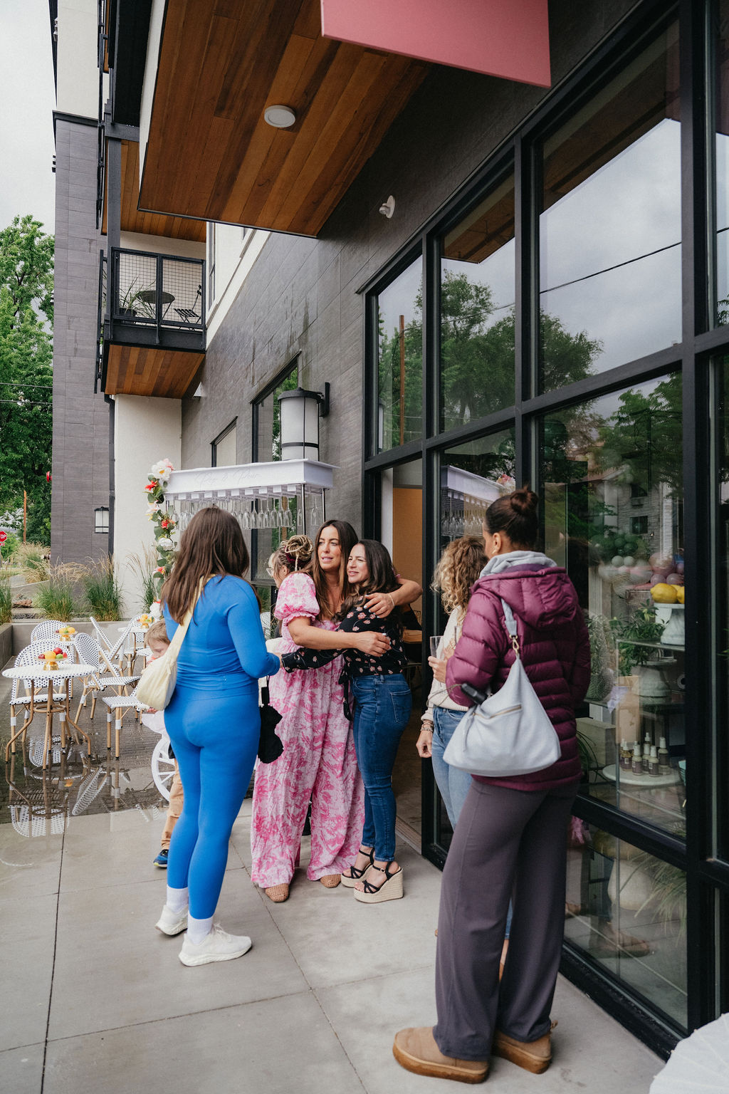 Four women stand outside a modern building with large glass windows, talking and smiling, with outdoor seating nearby.