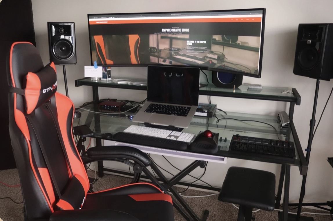 Computer desk with monitor, keyboard, mouse, speakers, and gaming chair in a room.