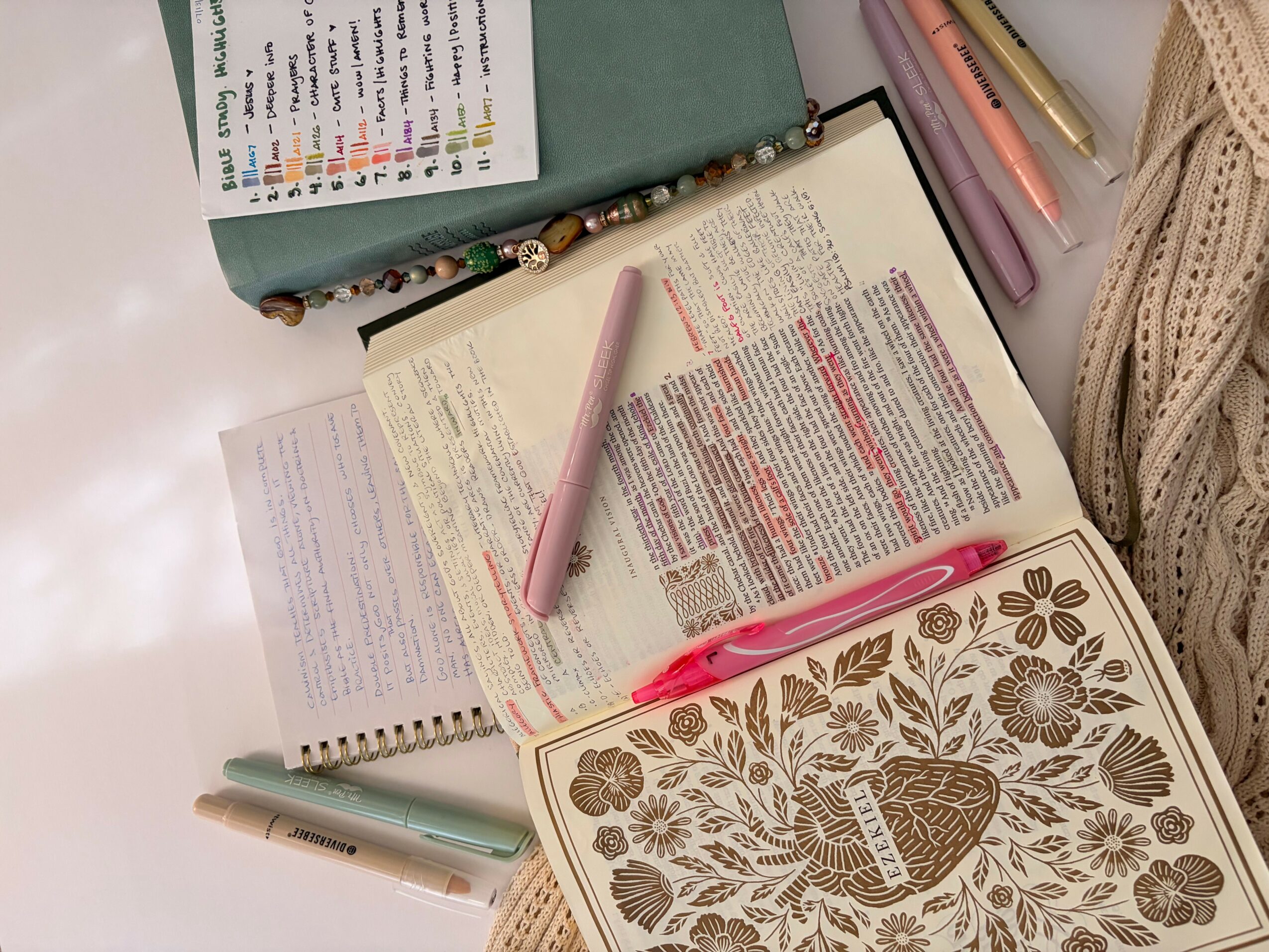 Open notebook with highlighted text, pink pen, and a closed notebook with floral cover on a desk.