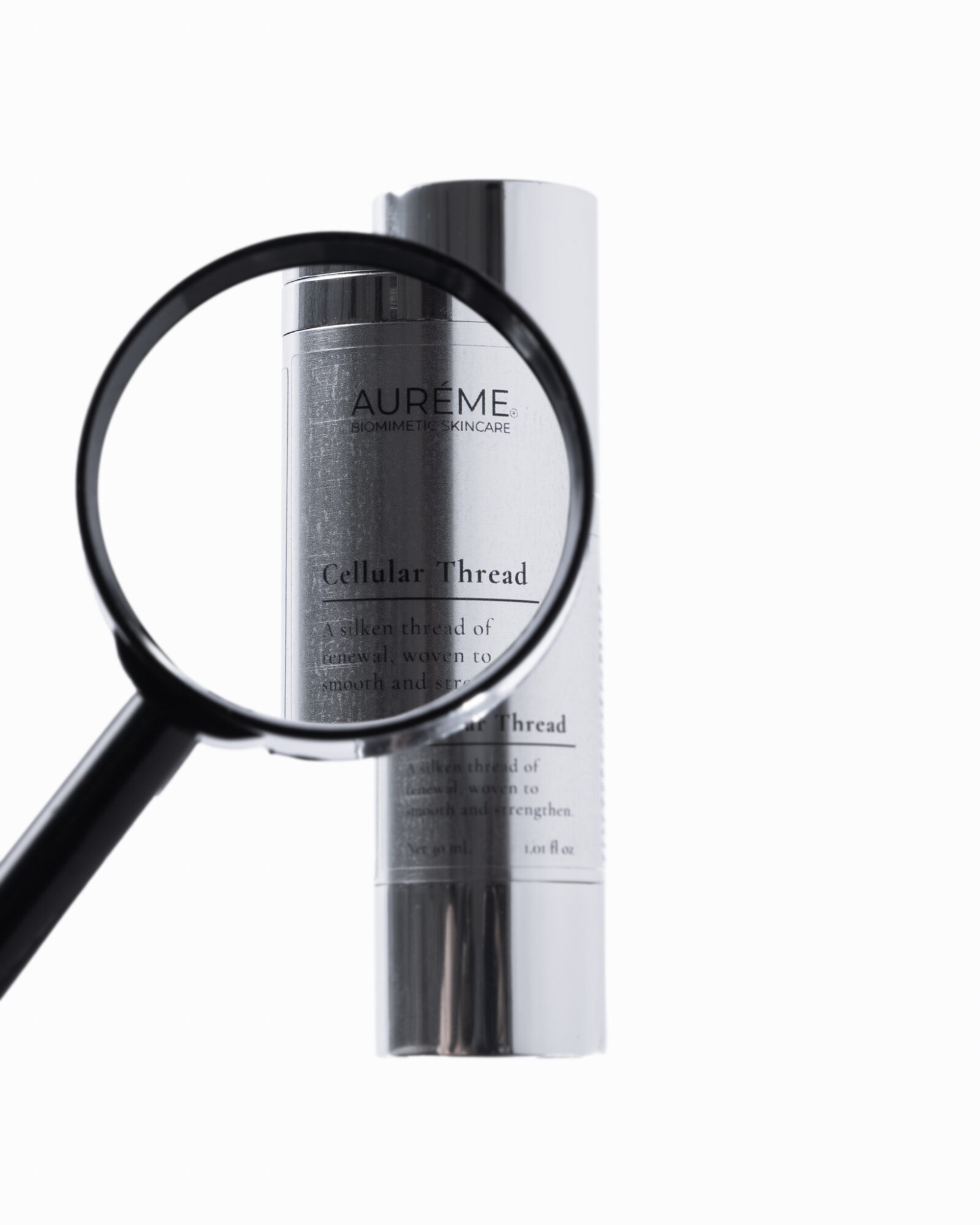 Magnifying glass focusing on a cylindrical skincare product with a white label, against a white background.