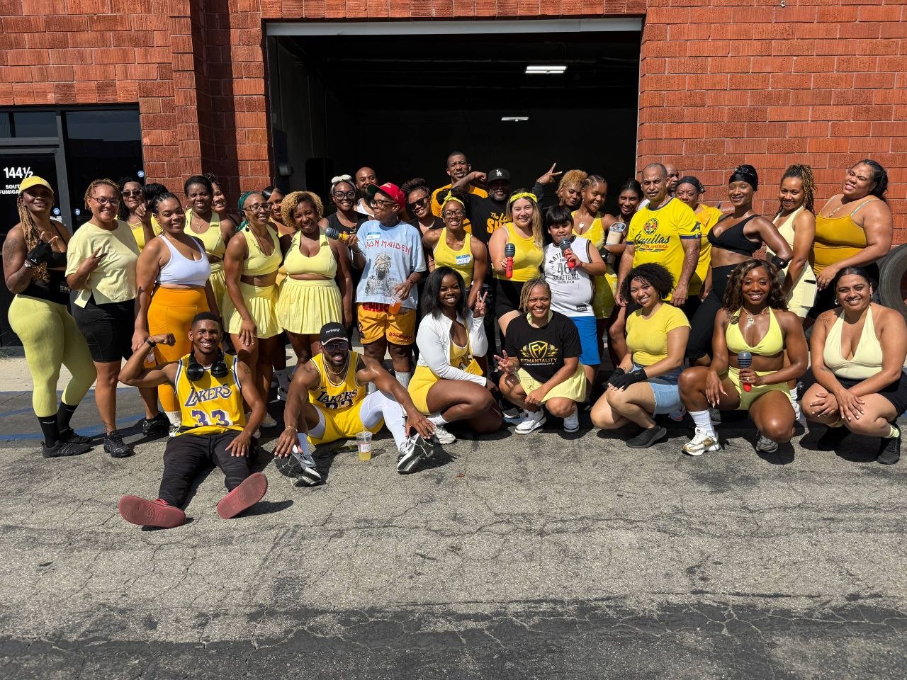 Group of people in yellow and black clothing standing and sitting outside a brick building, smiling and posing for a photo.