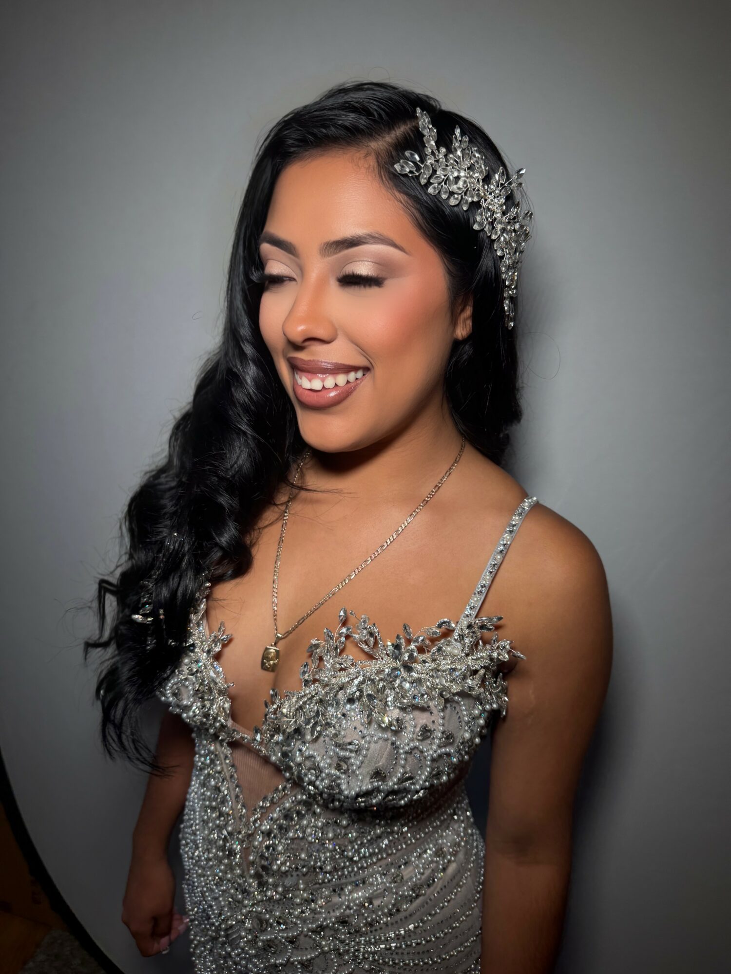 Woman with long dark hair wearing a silver, beaded dress and a decorative headpiece, smiling with eyes closed.